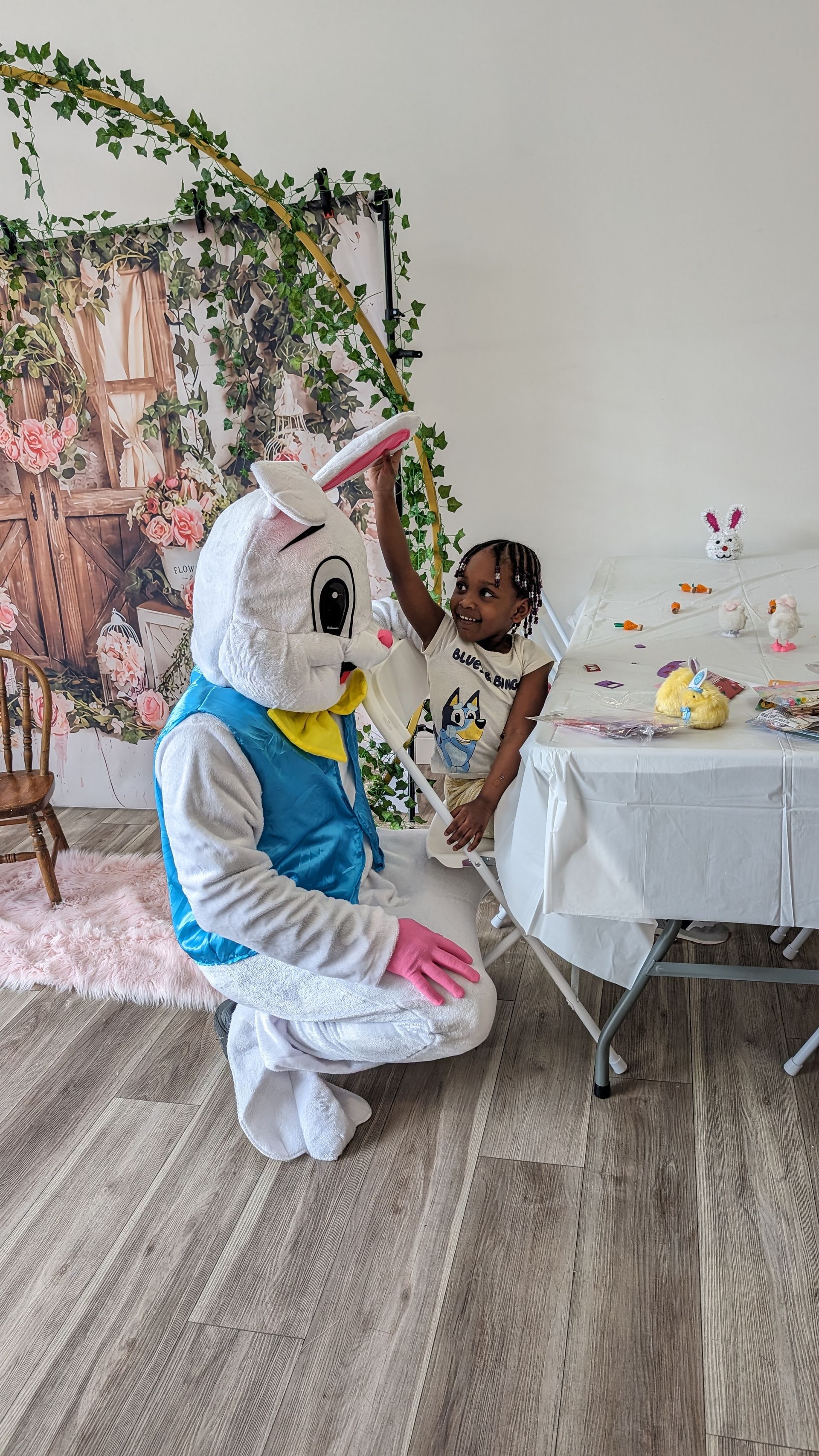 Person in white bunny costume kneels beside a child at a decorated party table with pastel decor