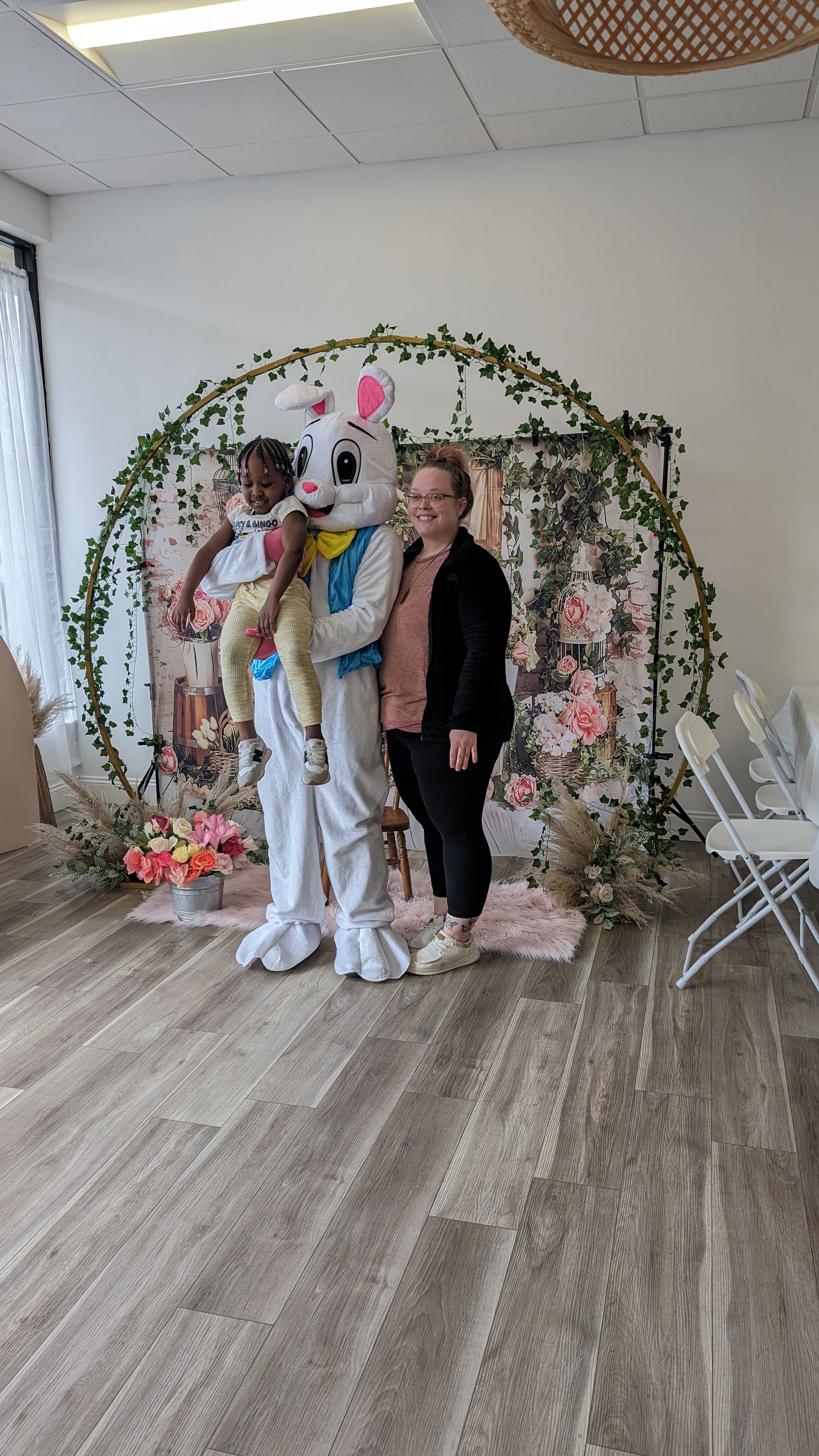 Three people posing beside a floral arch and balloons in a bright decorated room