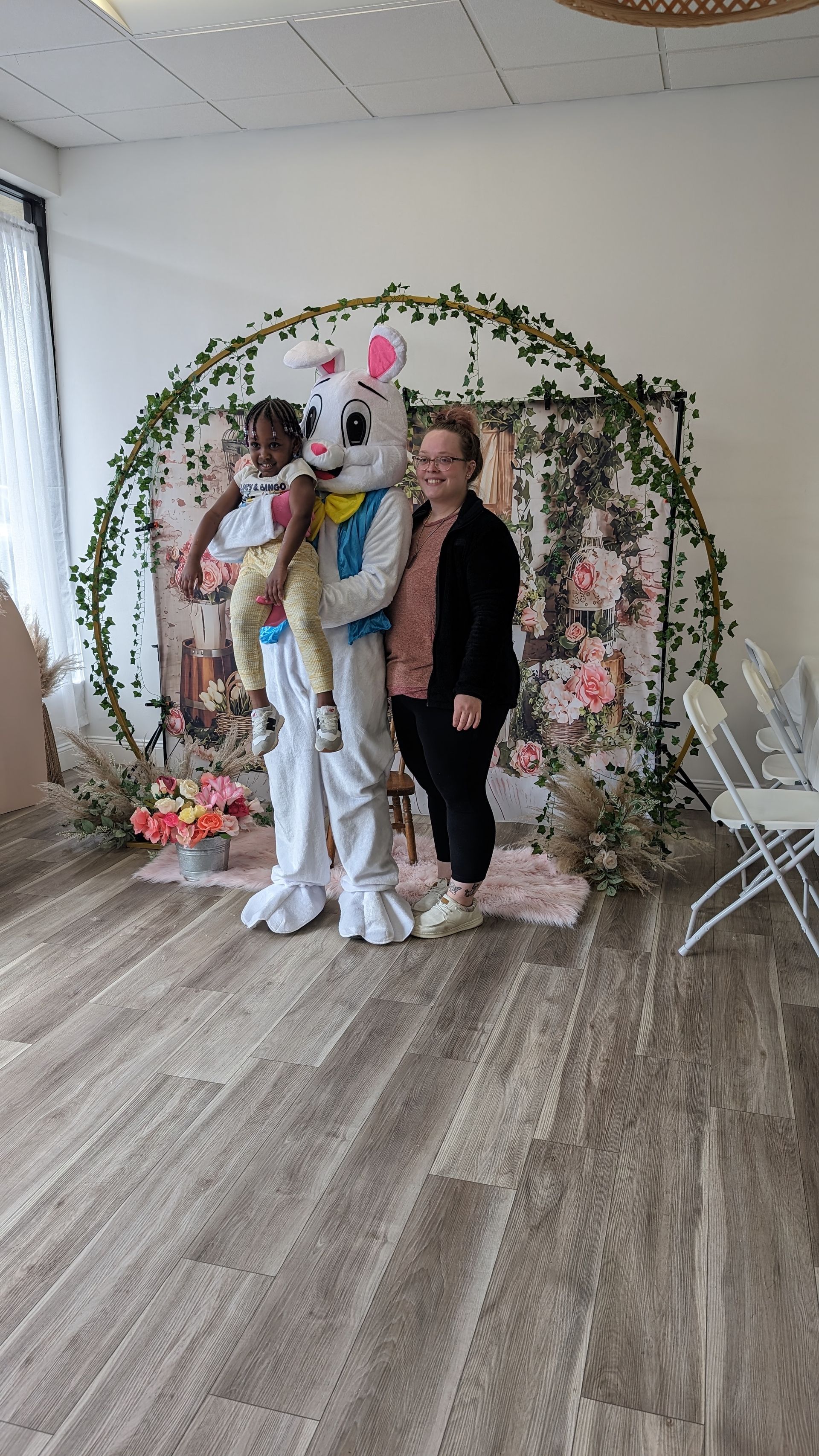 Three people posing in front of a flower-covered arch at a decorated event venue