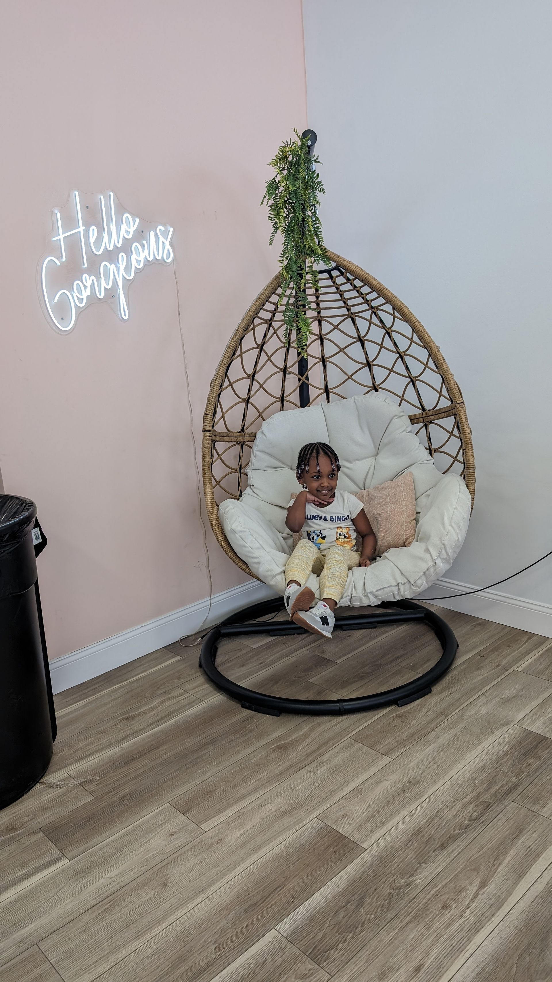 Baby sitting in a hanging wicker chair with a fluffy white cushion in a pastel room.