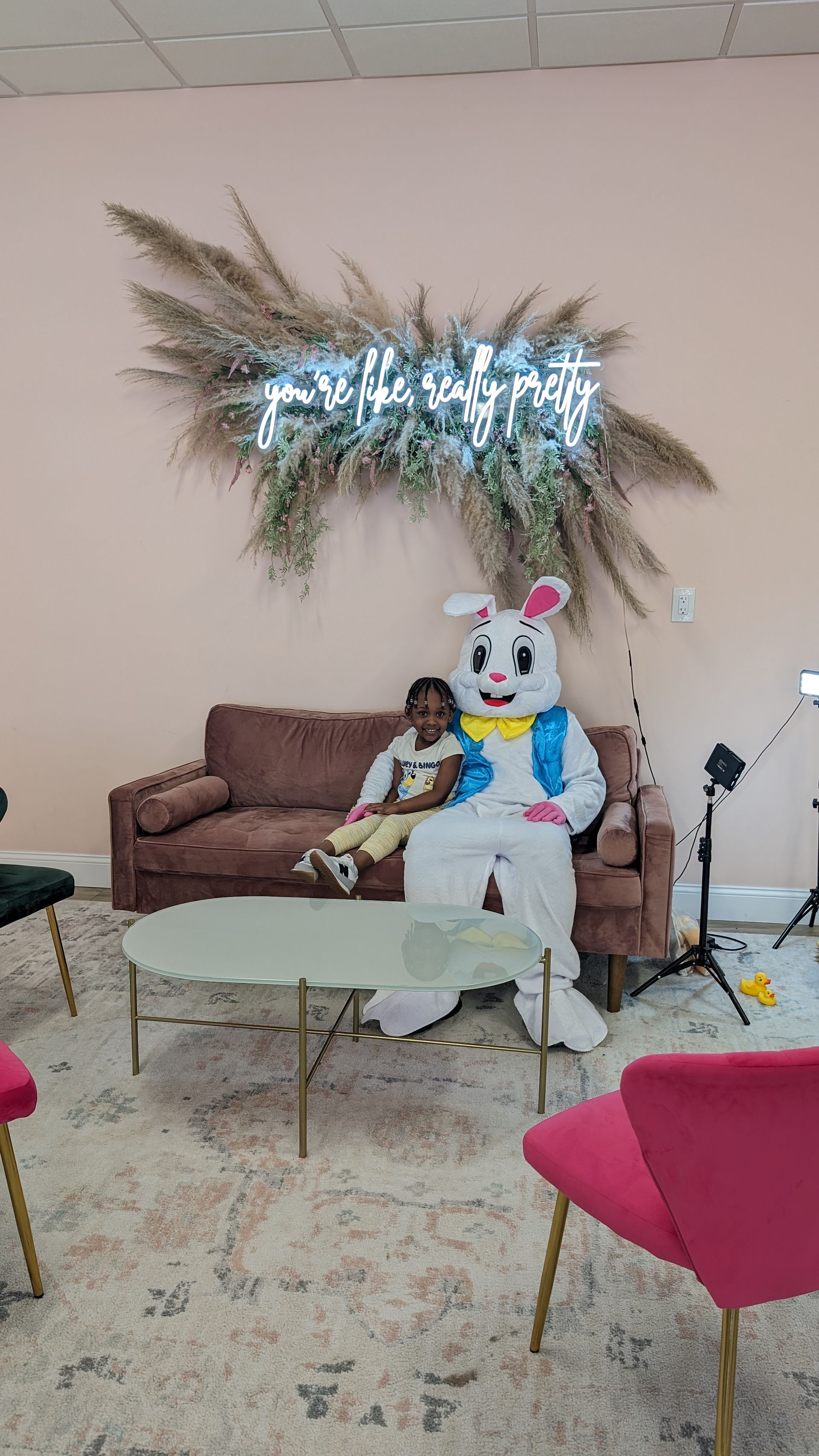 Living room with brown sofa, shiny wall decor, white rabbit figure, and colorful chairs around a glass coffee table