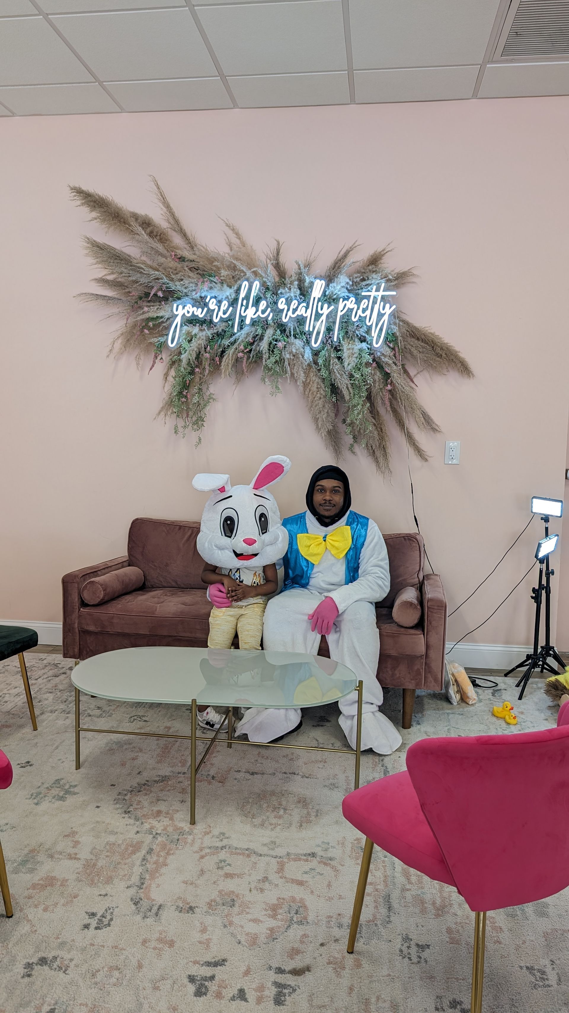 Person seated on a couch beside a large white bunny mascot in a decorated lounge area