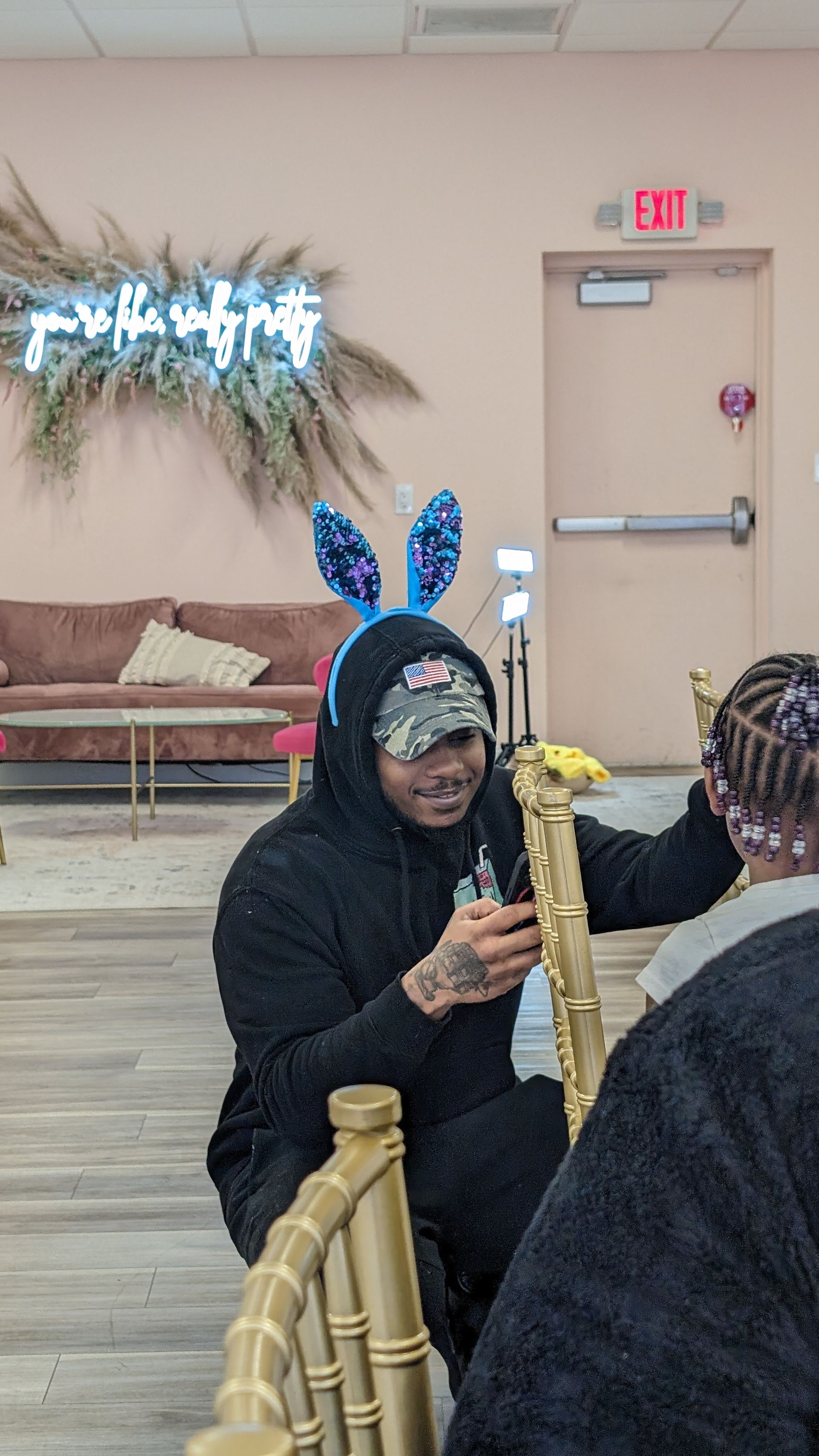 Person in blue bunny ears talking at a table in a decorated room with chairs and a closed door.