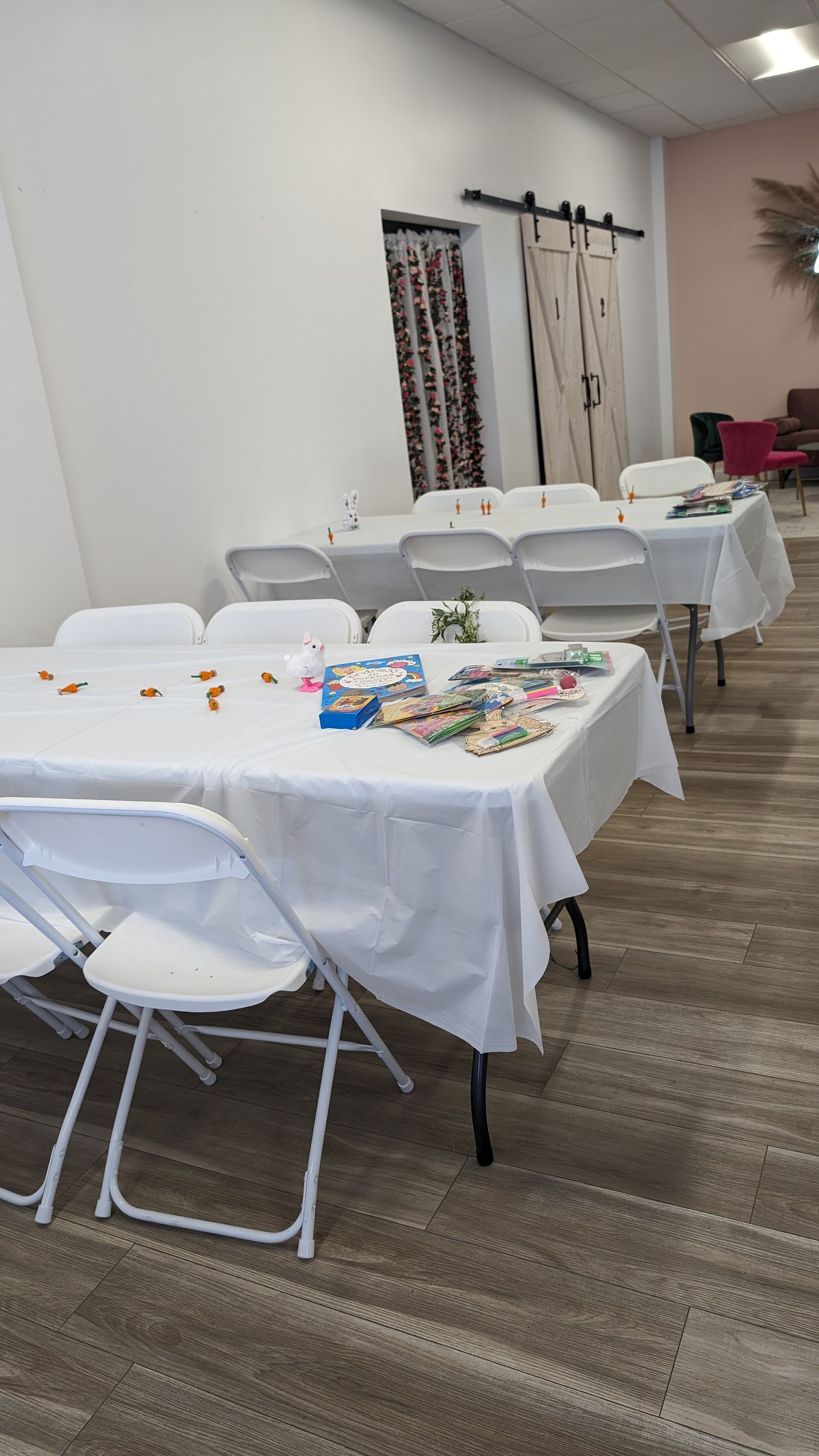 Rows of white-covered tables and folding chairs set up in a small event room, with party supplies on one table