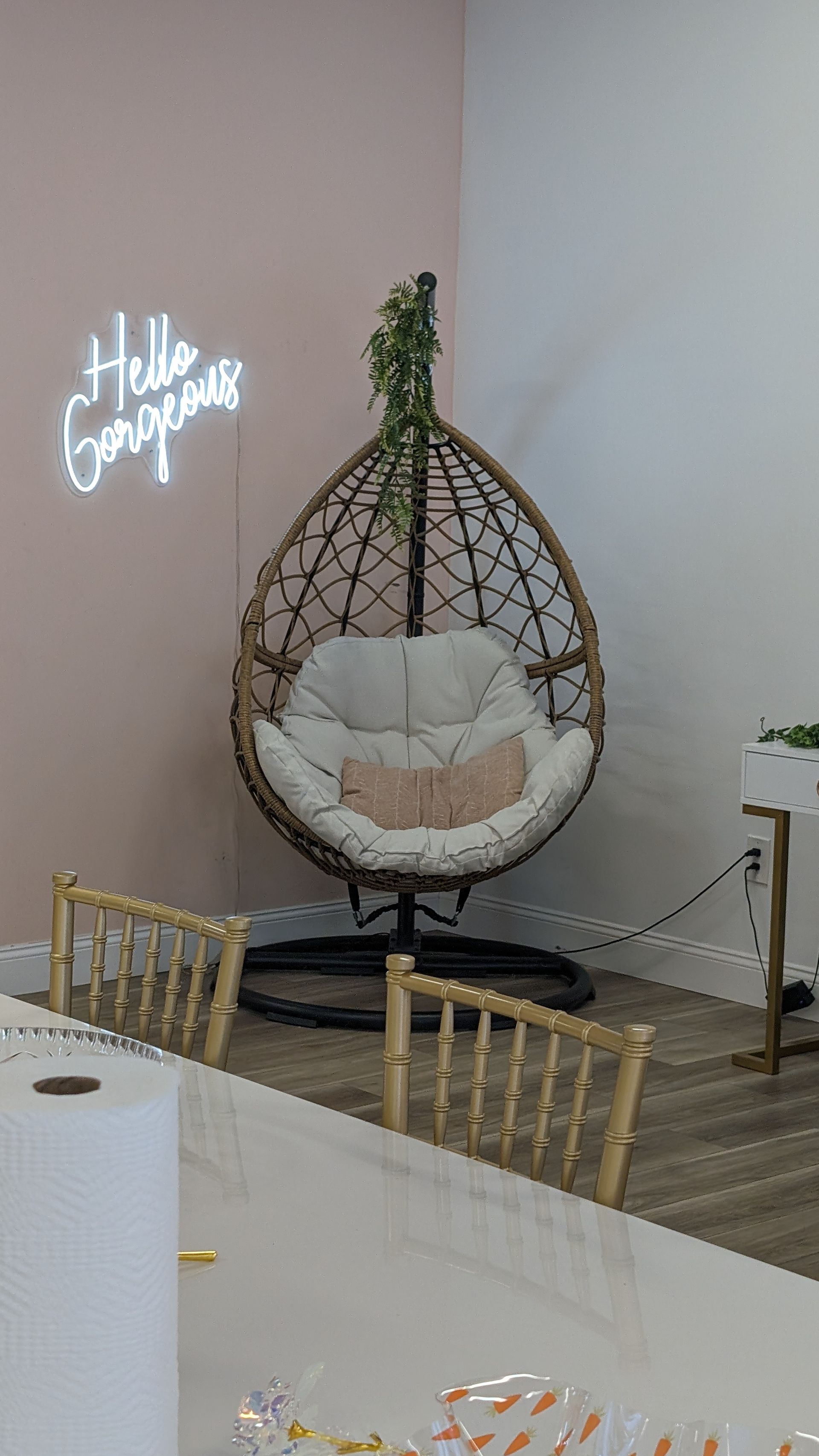 Indoor event lounge with a hanging egg chair, floral cushion, and neon “Happy Birthday” sign on the wall