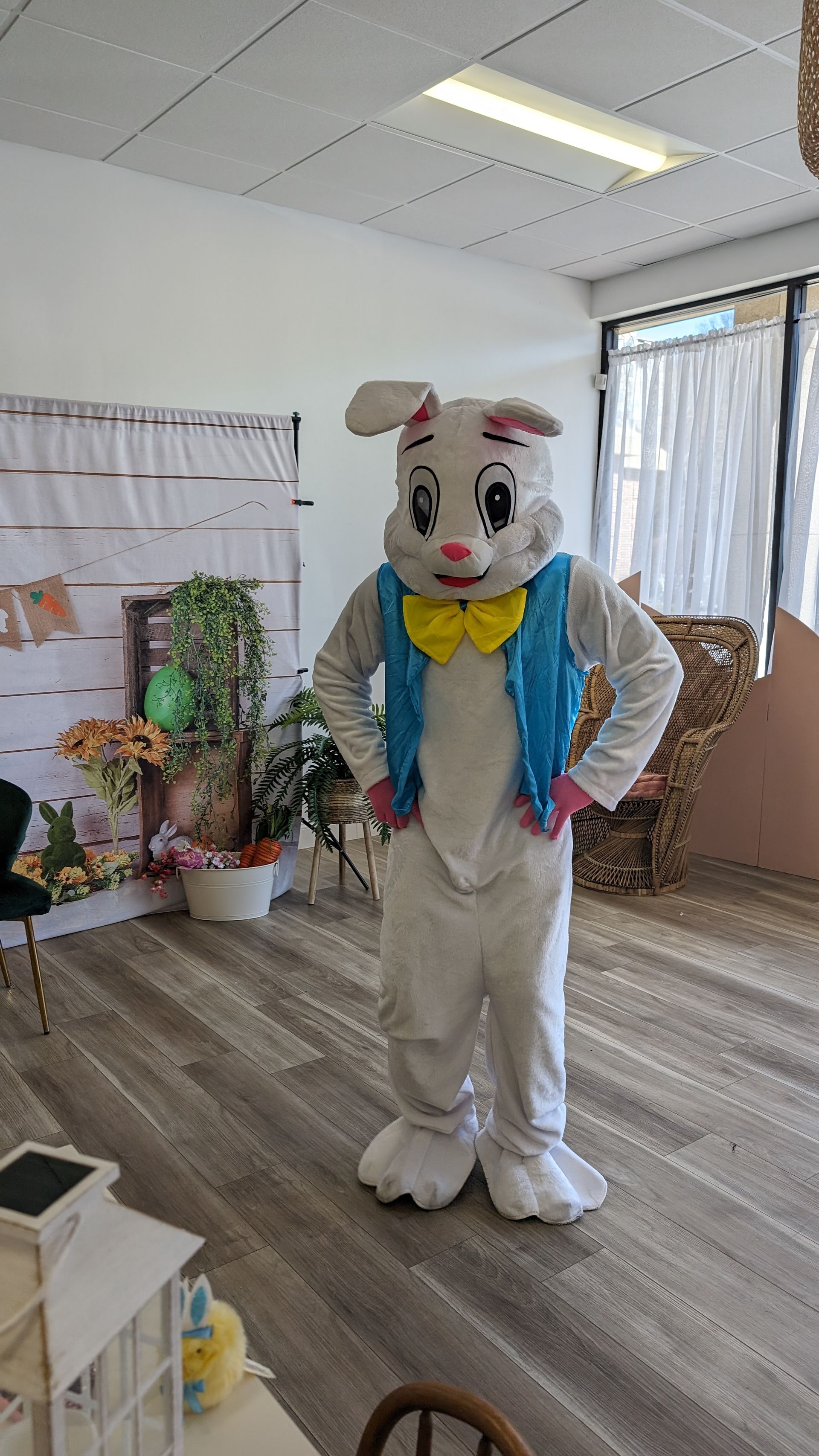 Person in a white bunny costume with a yellow bow tie stands in an office room.