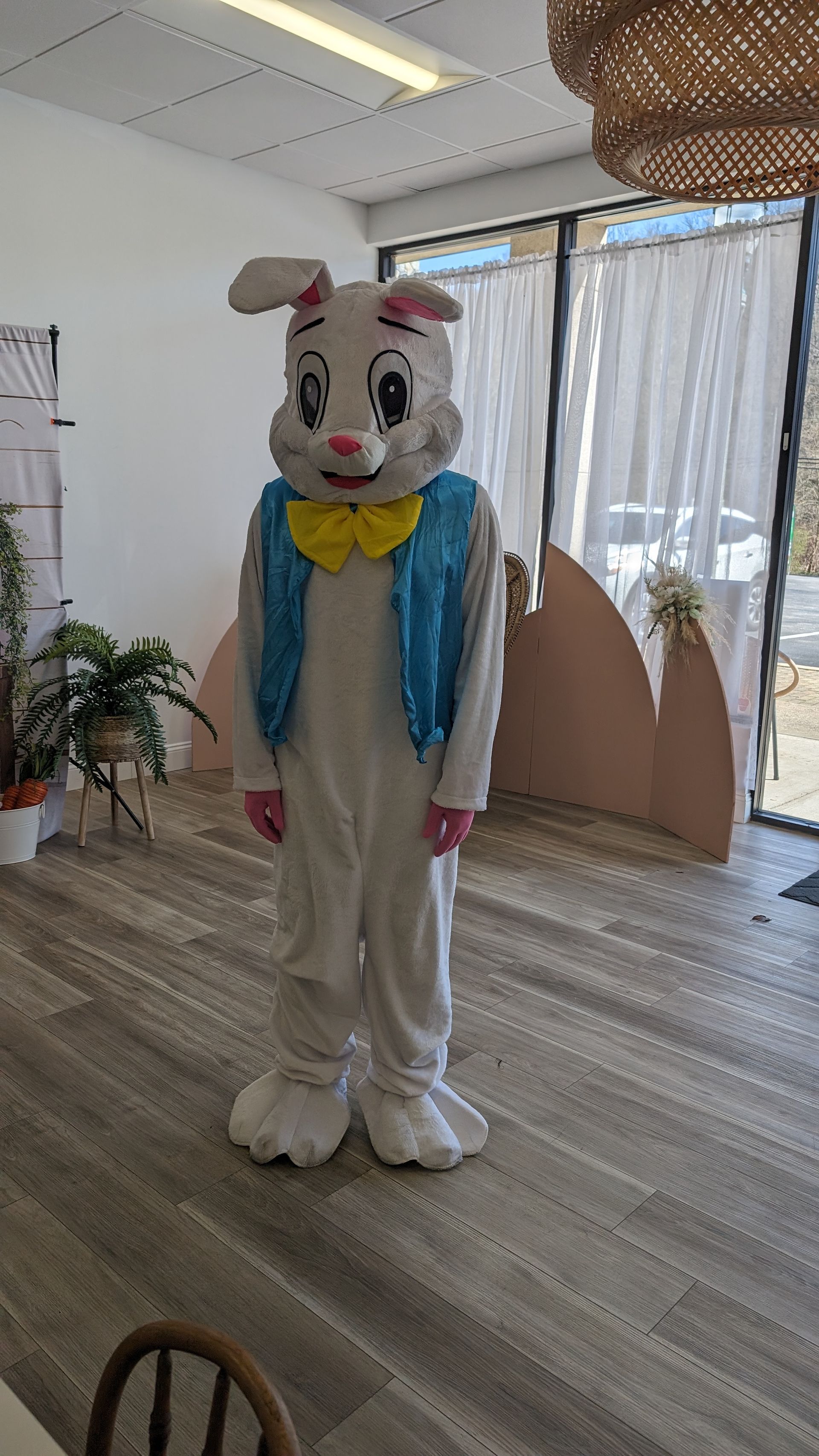 Person in a white bunny costume with blue jacket and yellow bow tie standing indoors.