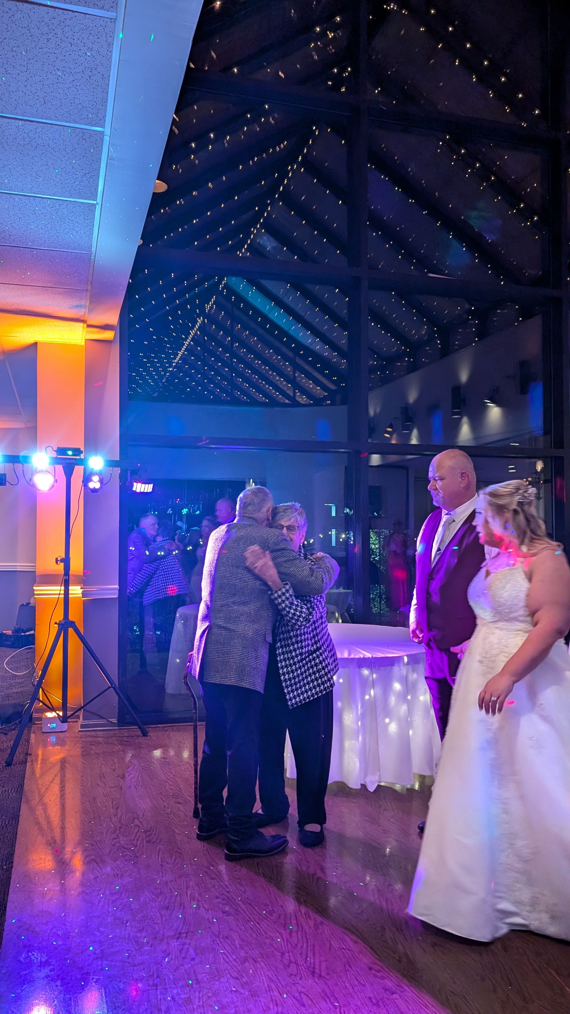 Wedding couple and officiant under lit pavilion, with purple and blue lighting at reception.