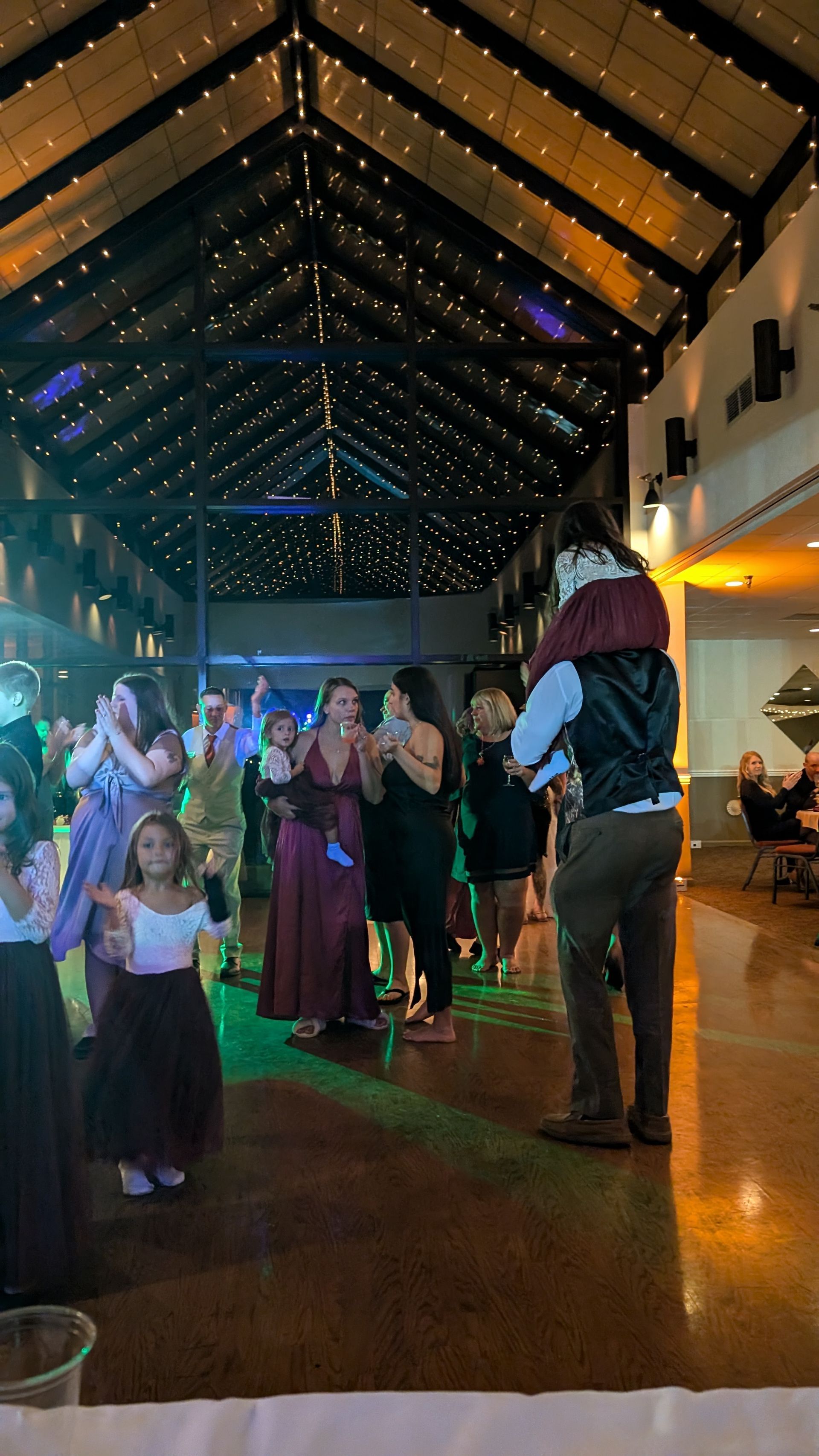 People dancing in a lit hall with a high wooden ceiling and colorful lights at a lively event