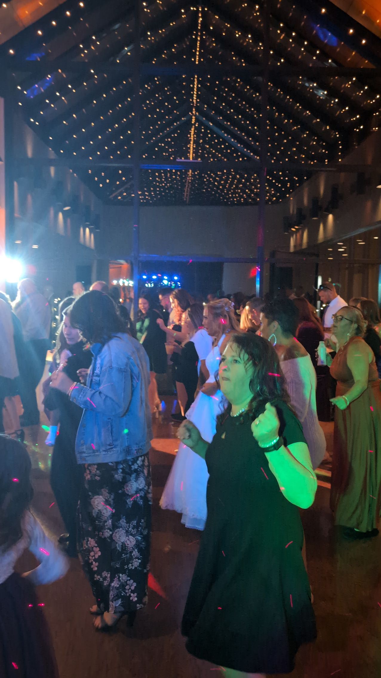 People dancing in a dimly lit venue with string lights overhead and colorful party lighting.