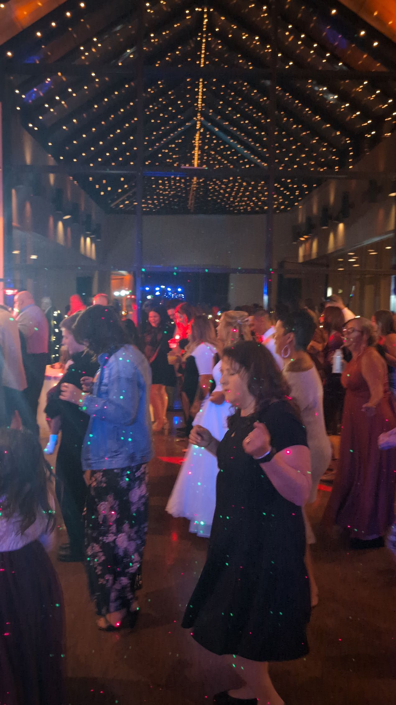 Crowded dance floor in a dimly lit hall with string lights on the ceiling and people dancing at a party