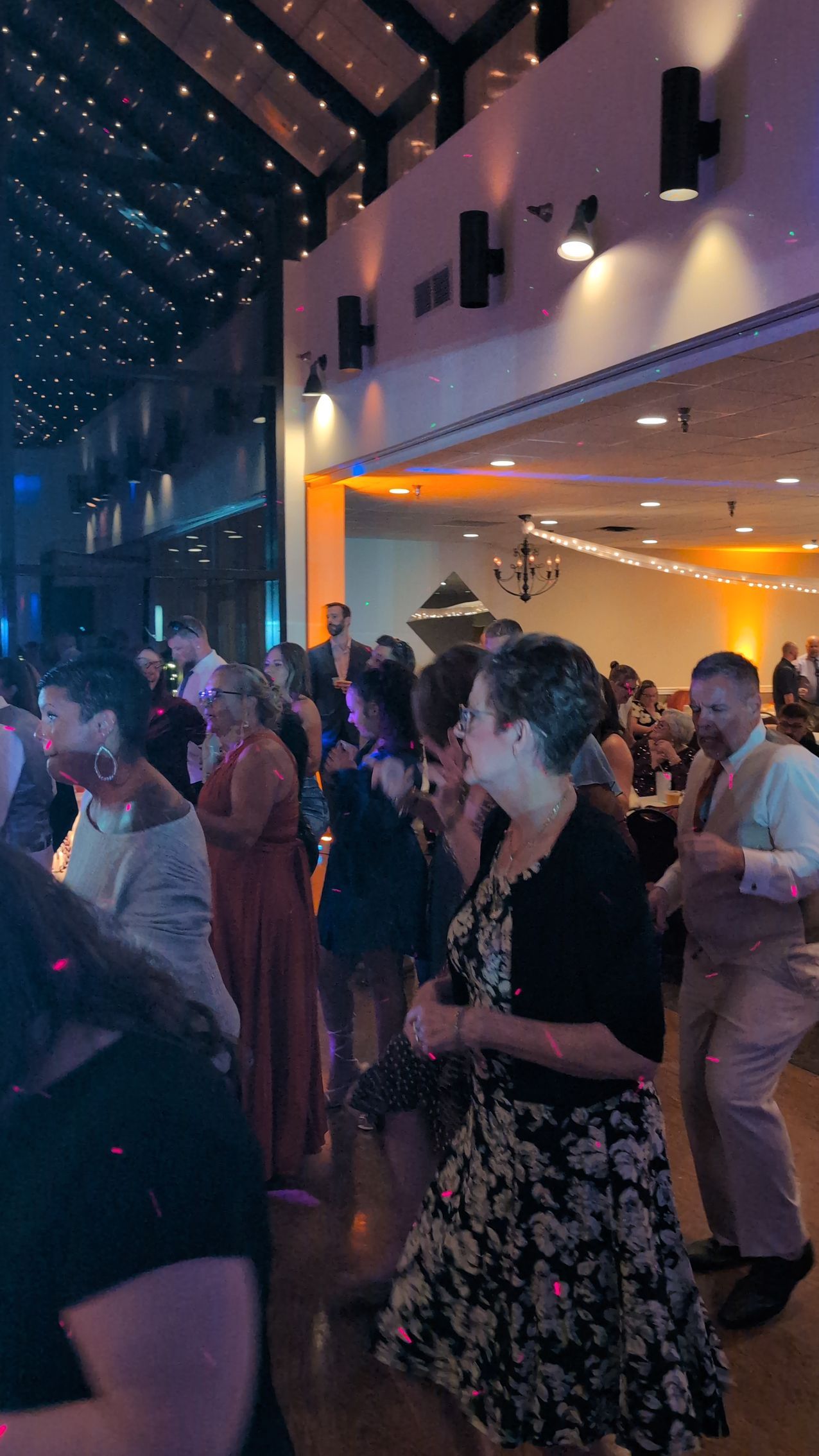 Crowd dancing in a modern indoor venue with warm orange lighting and a high ceiling