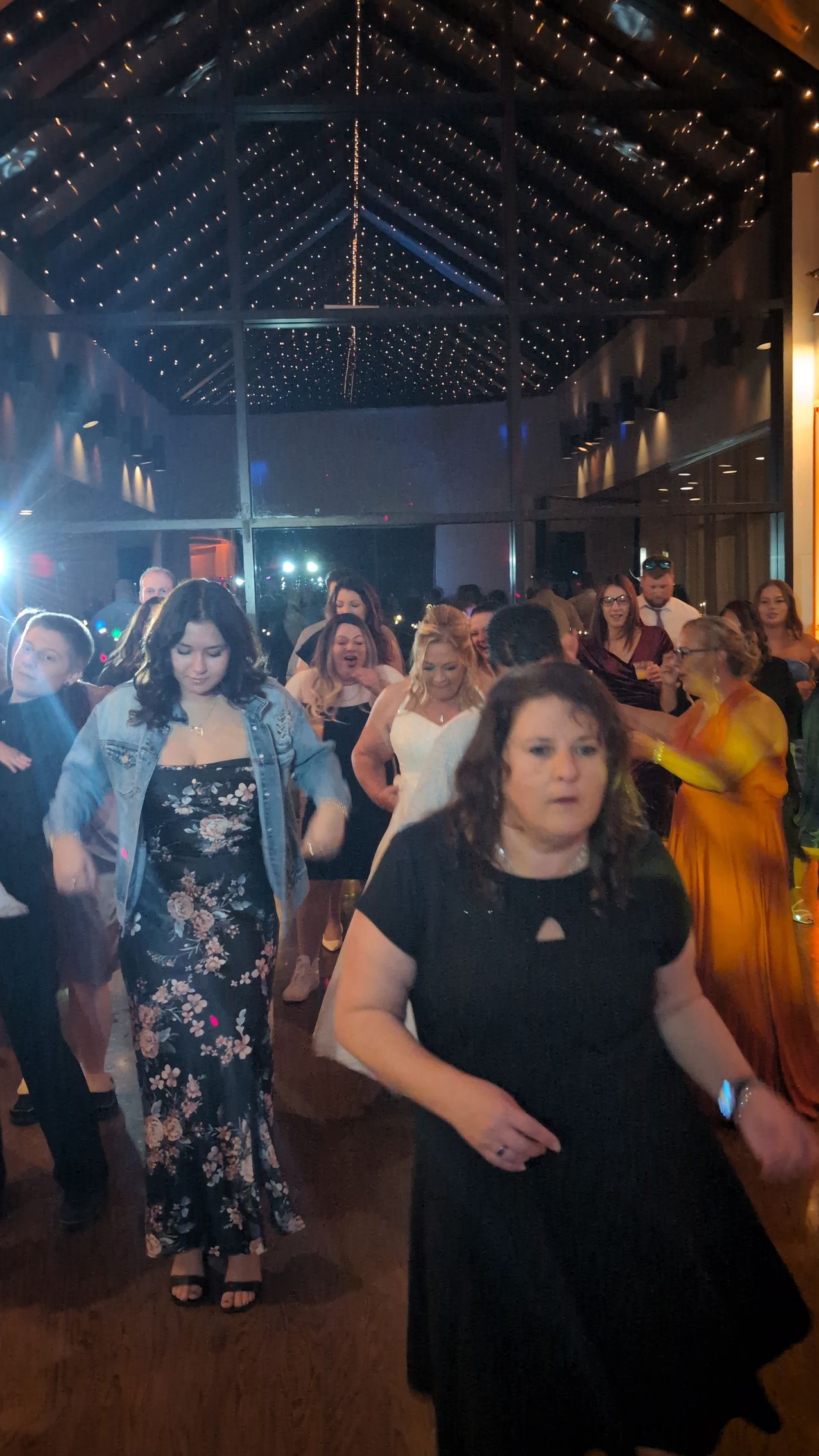 People dancing in a dimly lit hall with a high wooden ceiling and string lights overhead
