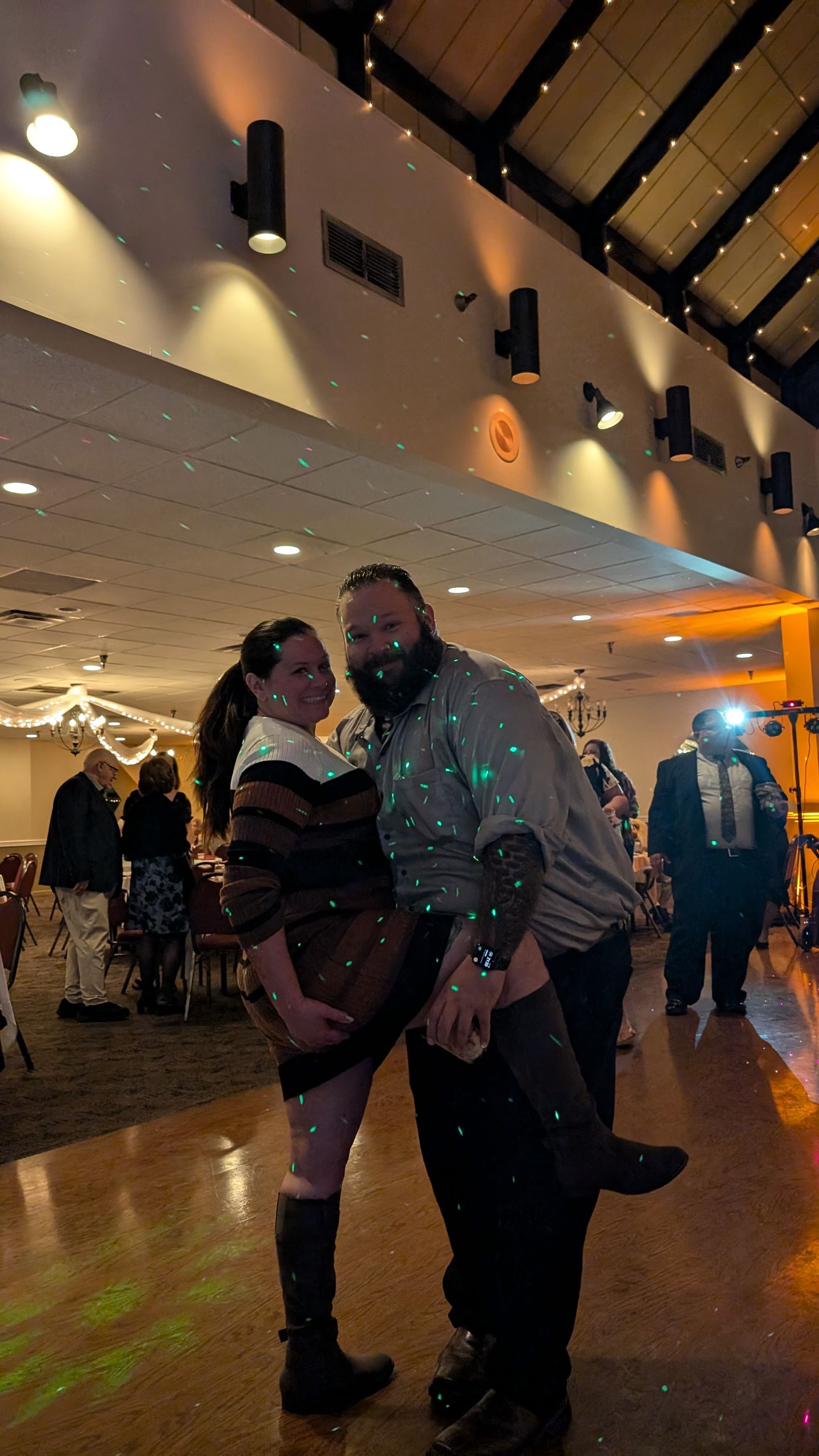 Two people posing together on a dance floor at a warmly lit indoor event.