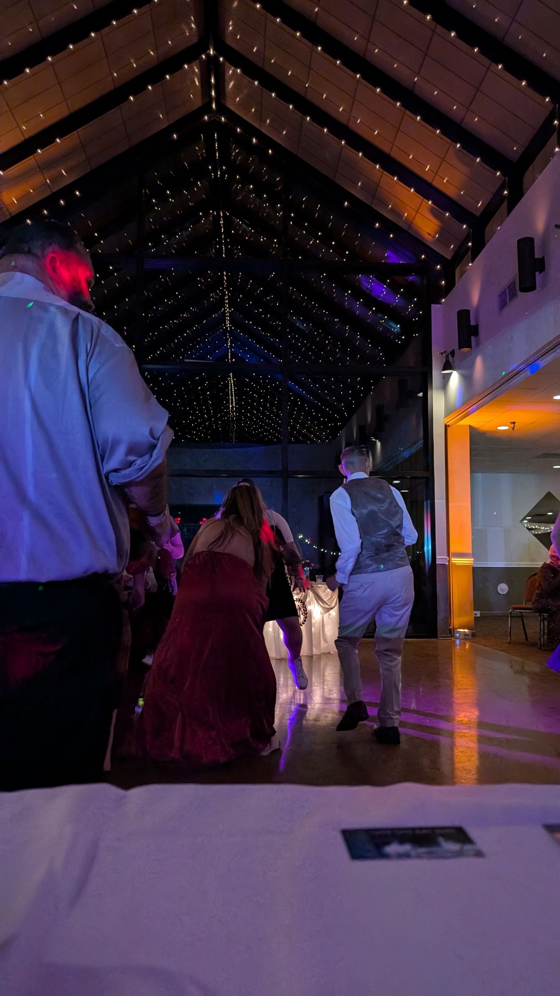 People dancing in a dimly lit hall with a starry ceiling and purple lighting.