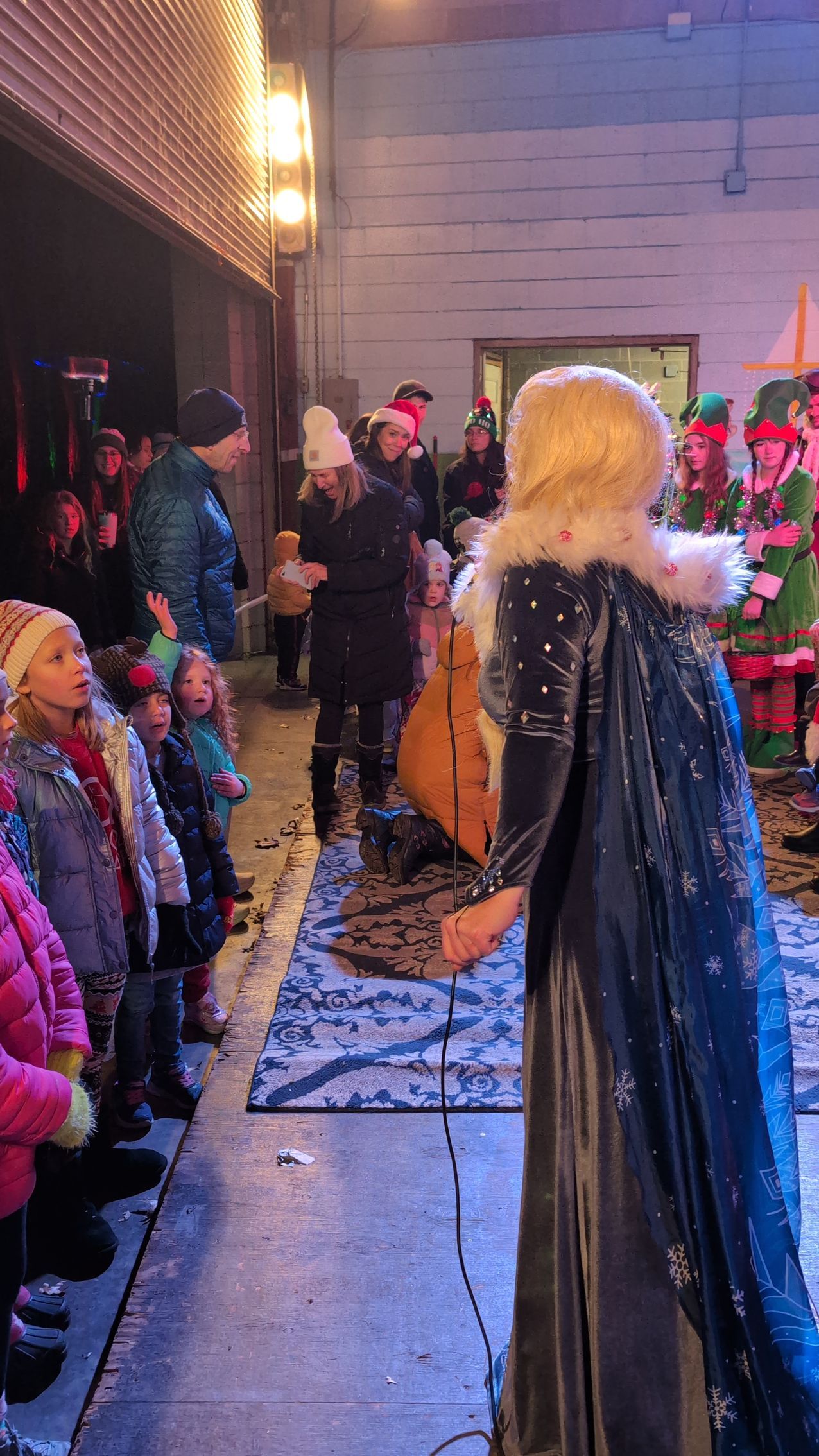 Costumed performer in a black cape faces a small crowd beside a decorated outdoor stage at night