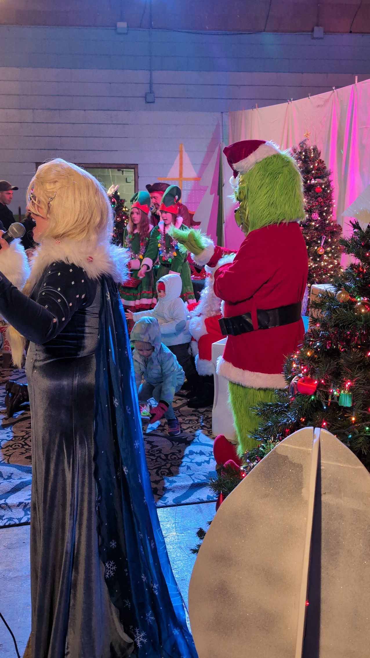 Holiday display with a blonde figure and a green Grinch-like figure among decorated Christmas trees
