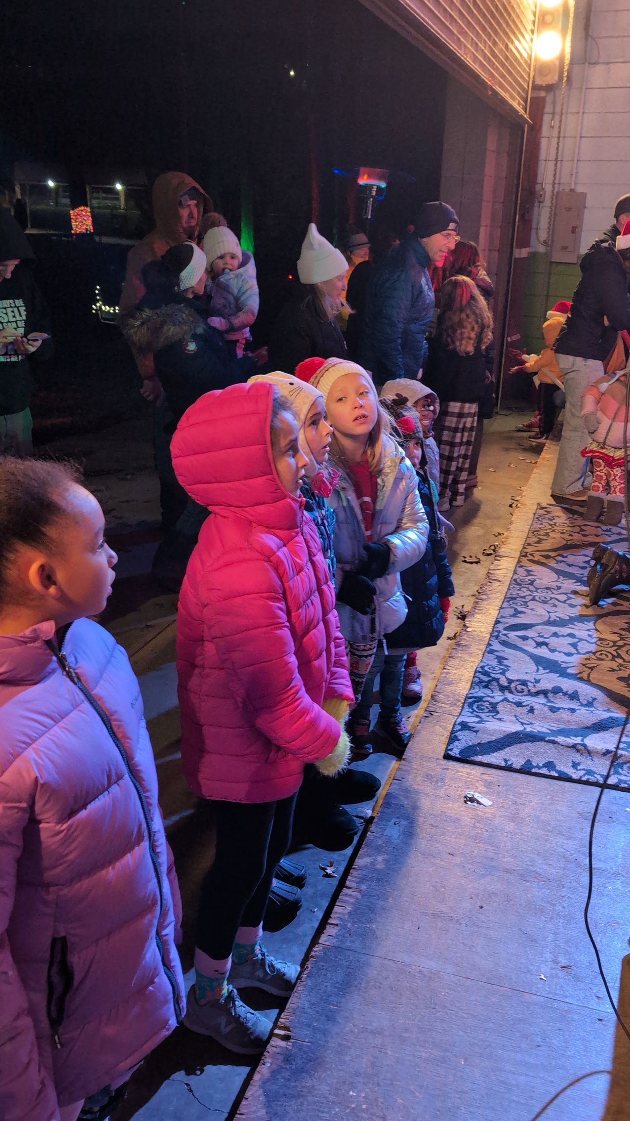 Children in winter coats standing in line outside a building at night
