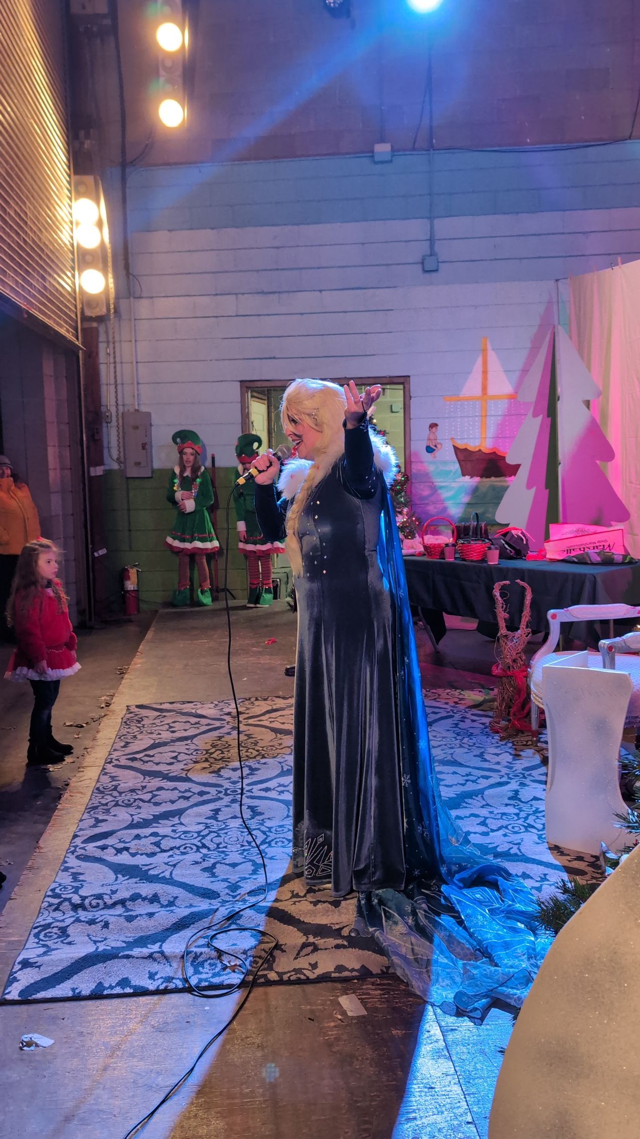 Singer in a long black dress performing on a decorated indoor stage with pink lighting.
