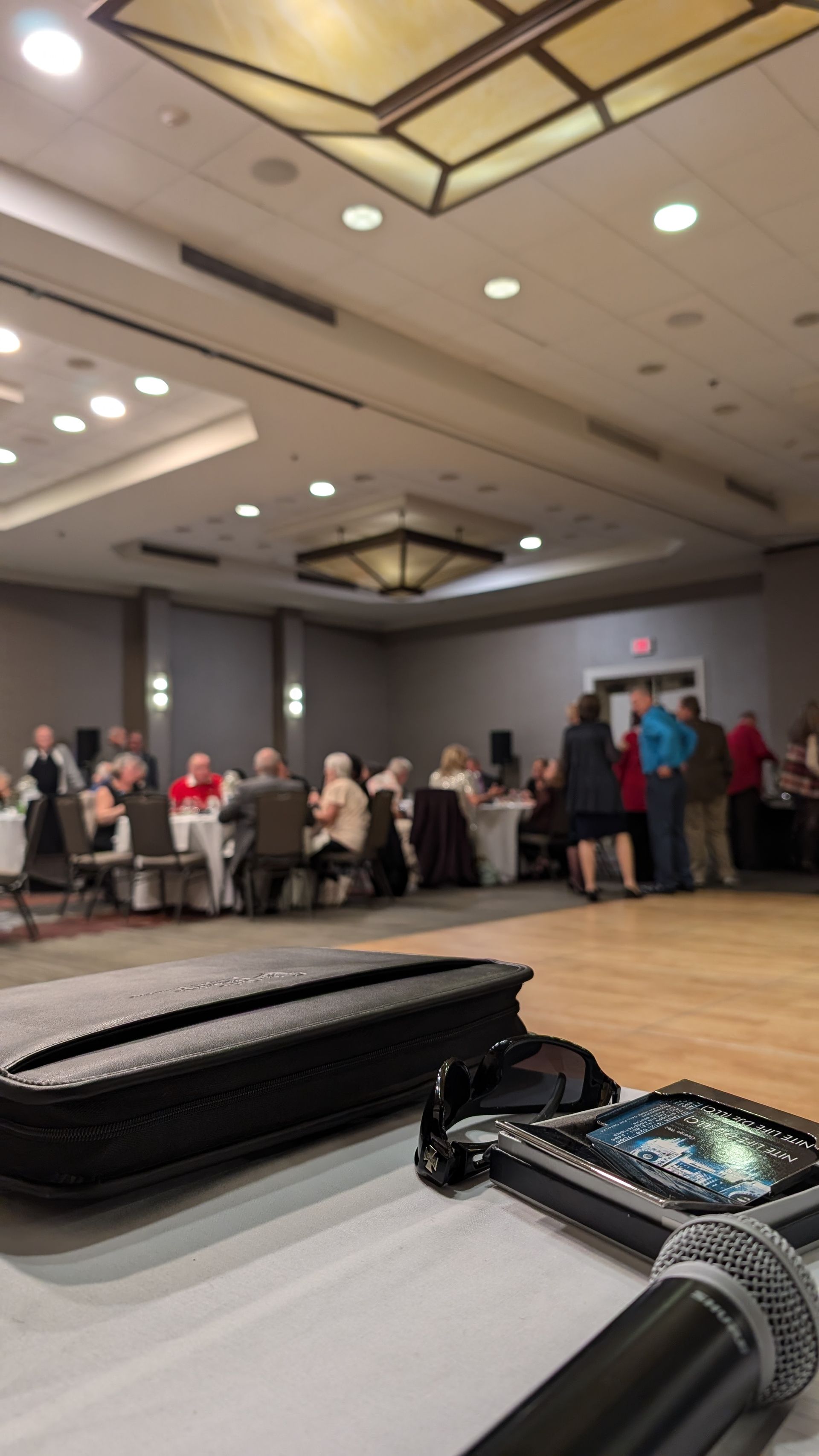 Banquet hall with seated guests at tables, viewed from a table with a watch in the foreground.
