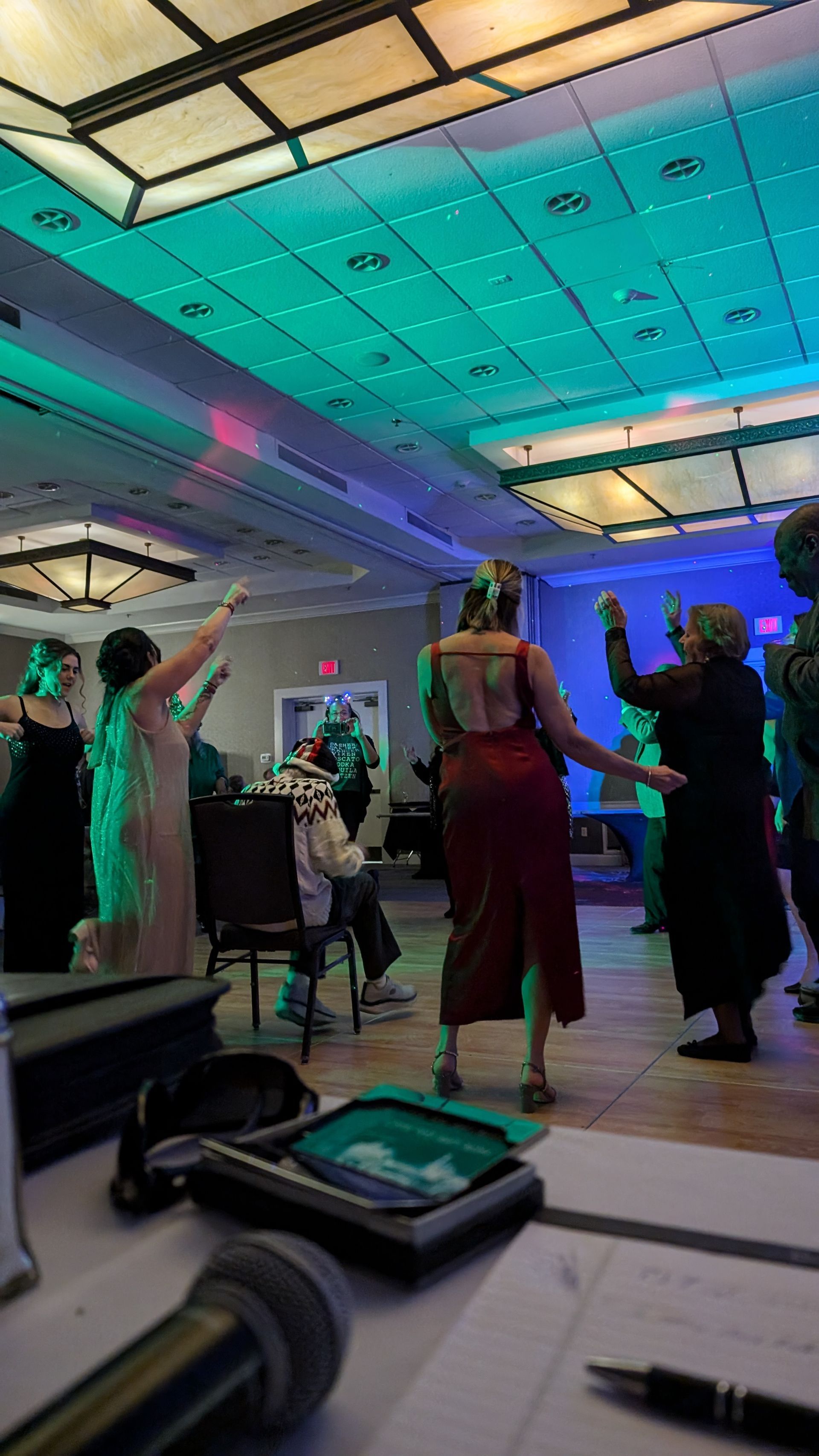 People dancing at a colorful indoor party under a teal-lit ceiling
