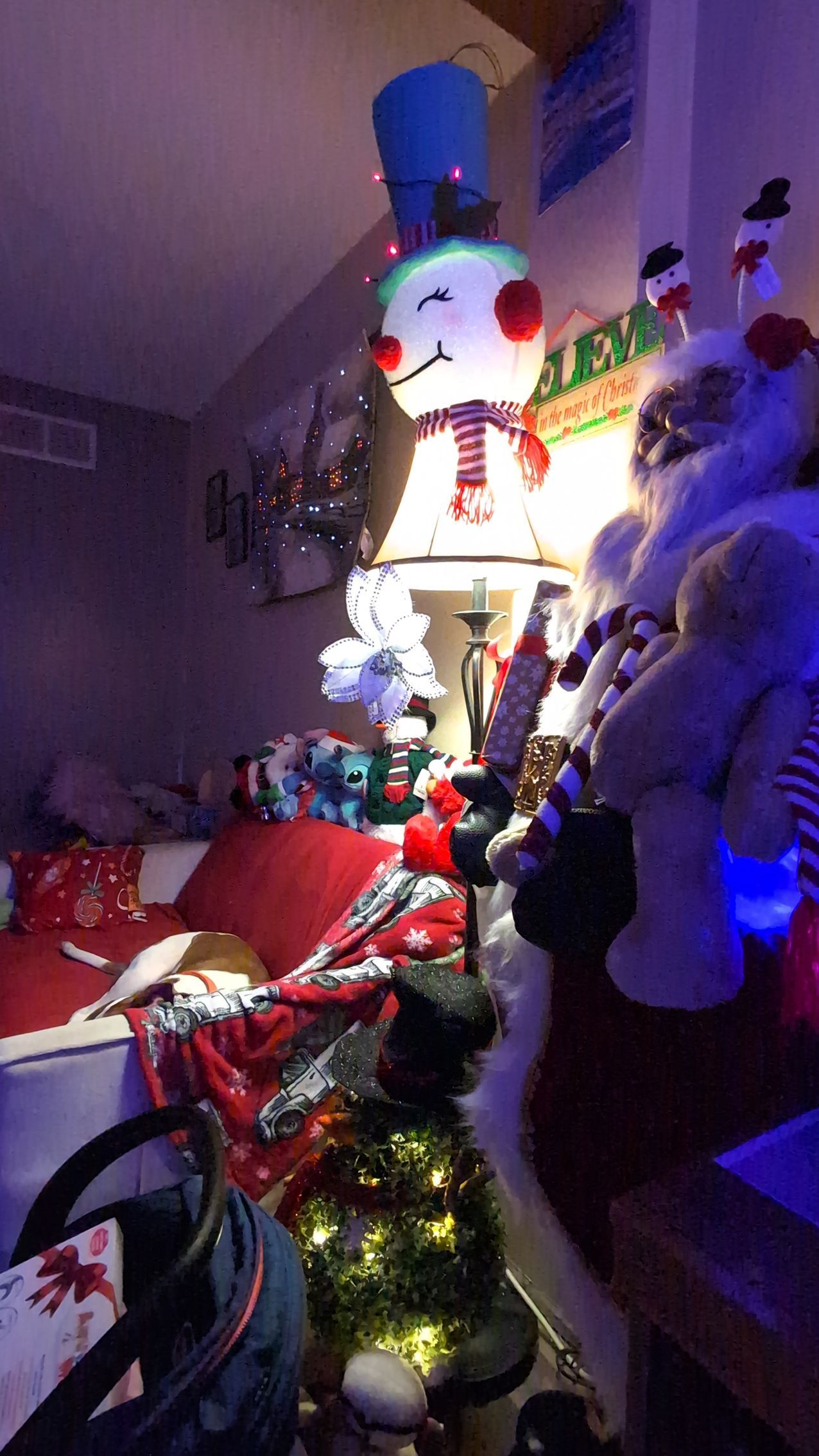 A decorated snowman display with lights, ornaments, and stuffed animals on a shelf in a festive room.