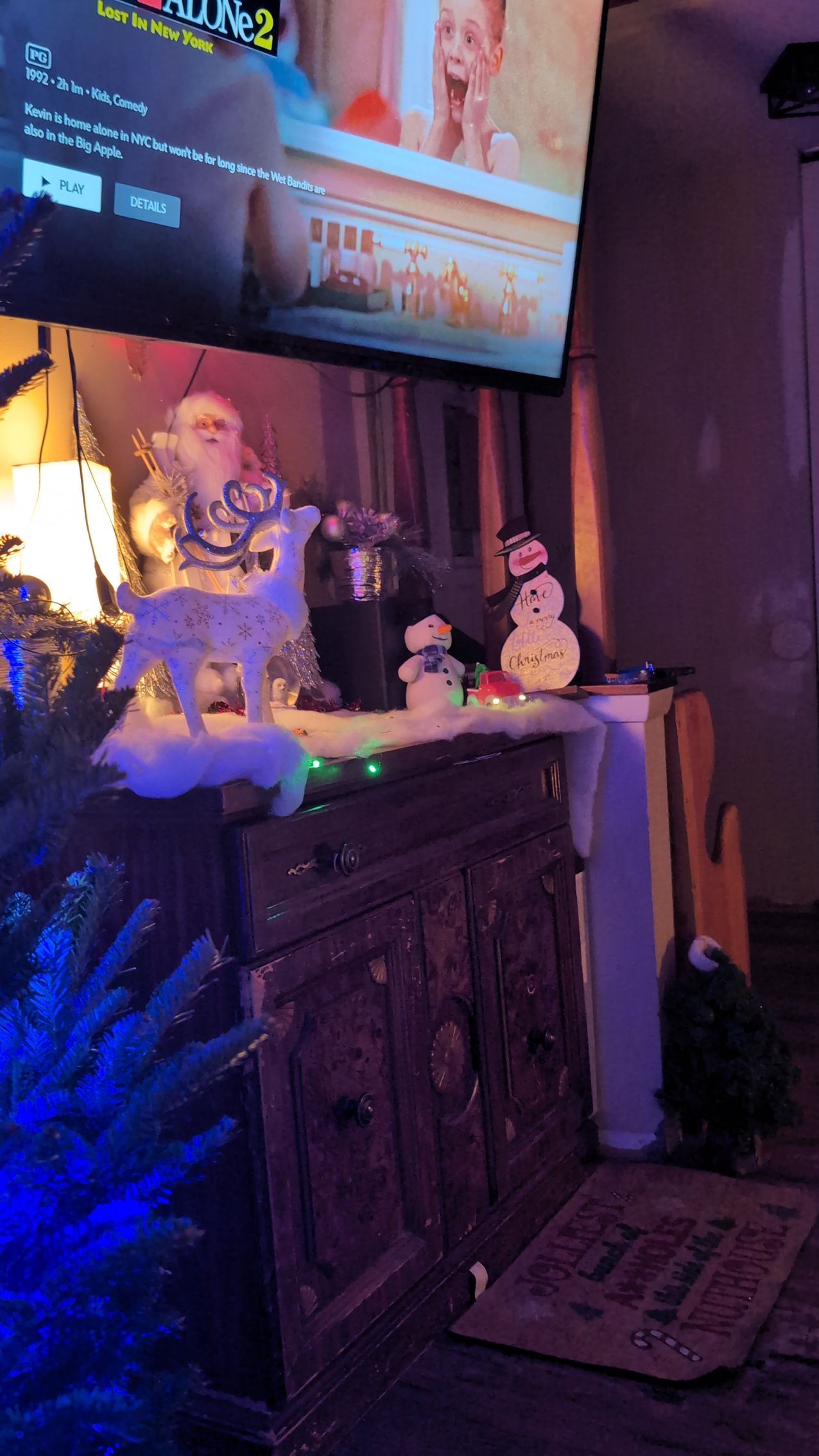 Colorful holiday mantel display with glowing lights, Santa figurine, and a TV above a fireplace.