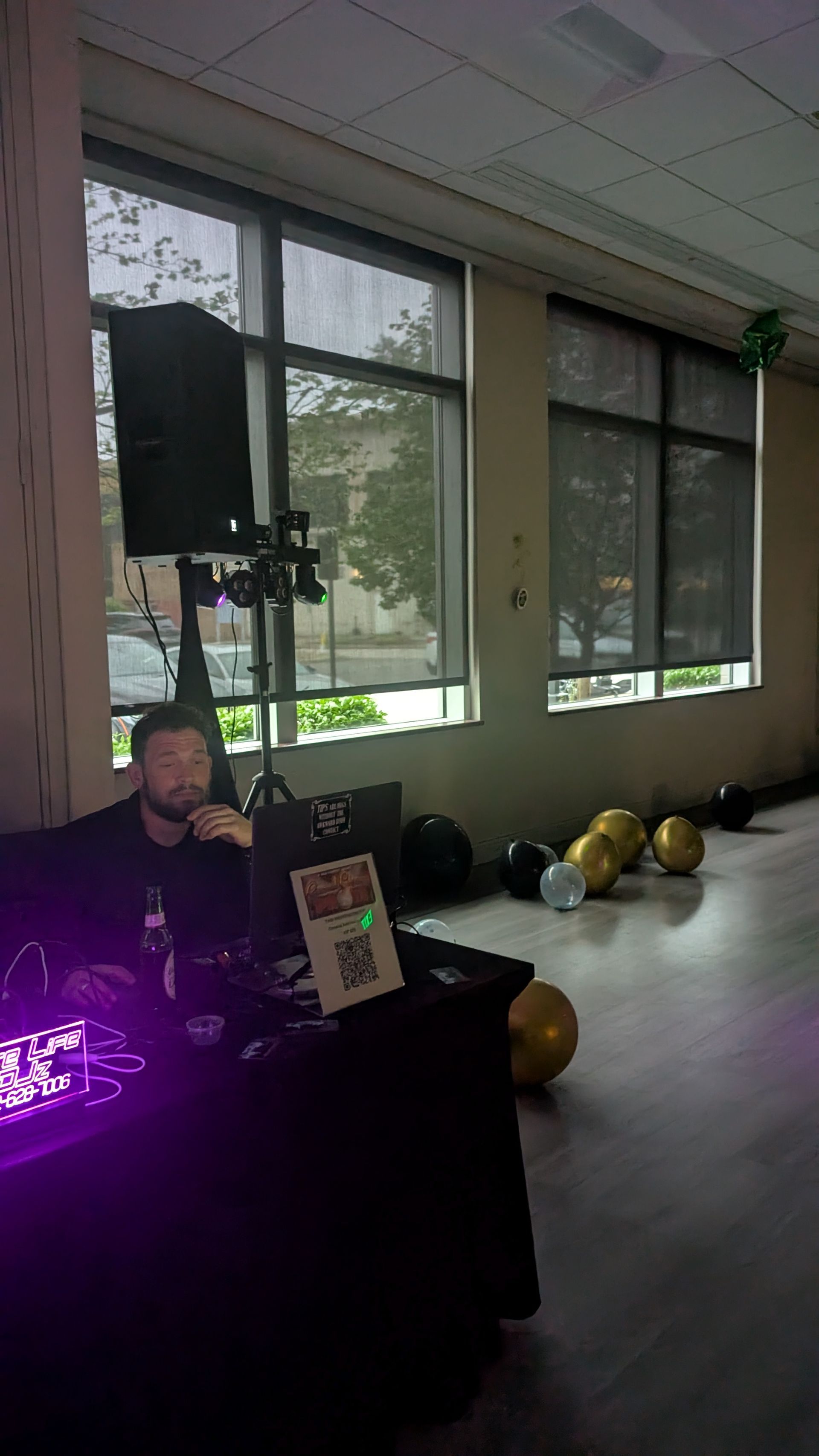 Event booth with a person seated at a black table beside a glowing purple light and windowed room backdrop