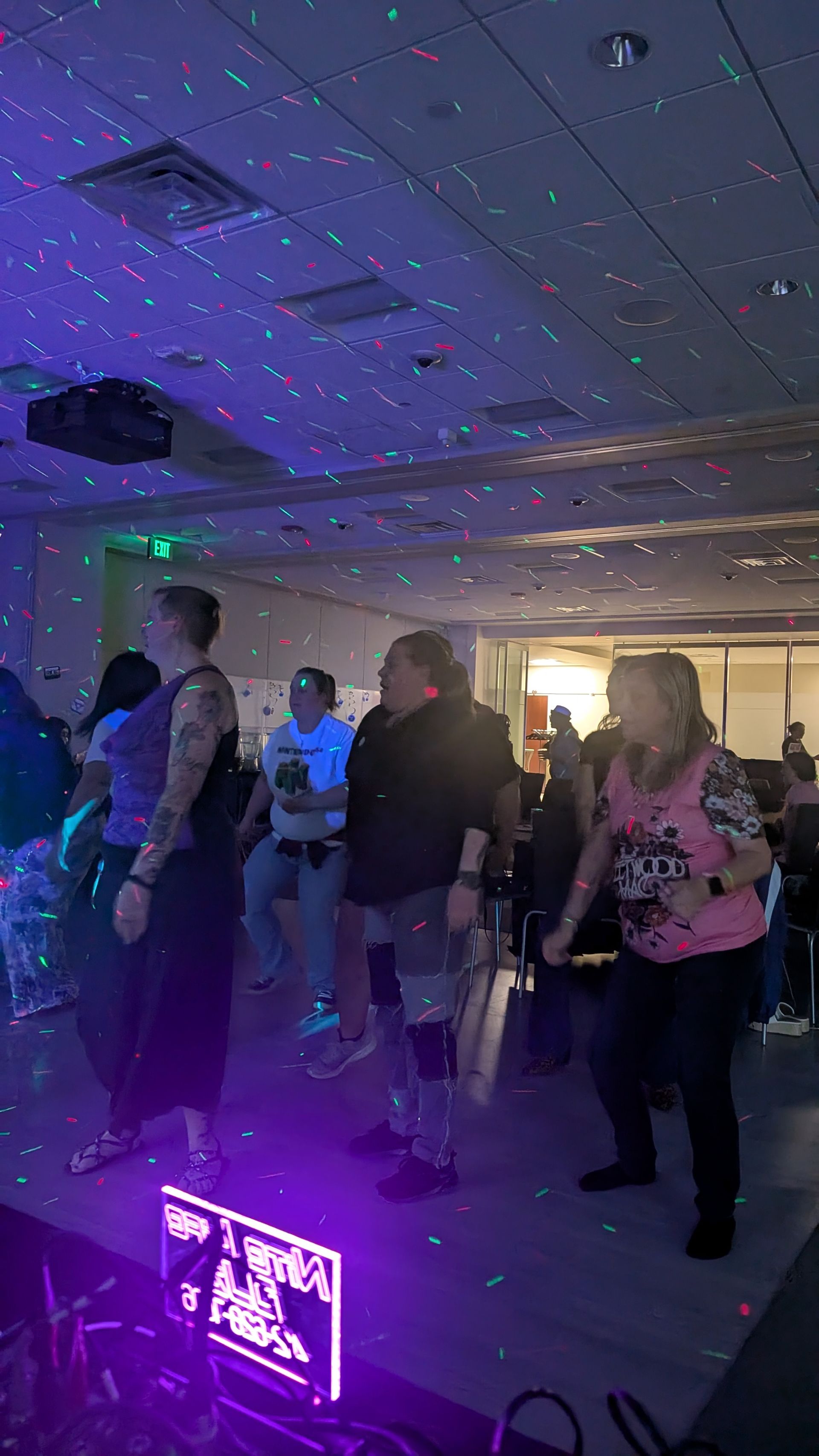 People dancing in a dimly lit room with purple lights at a social event