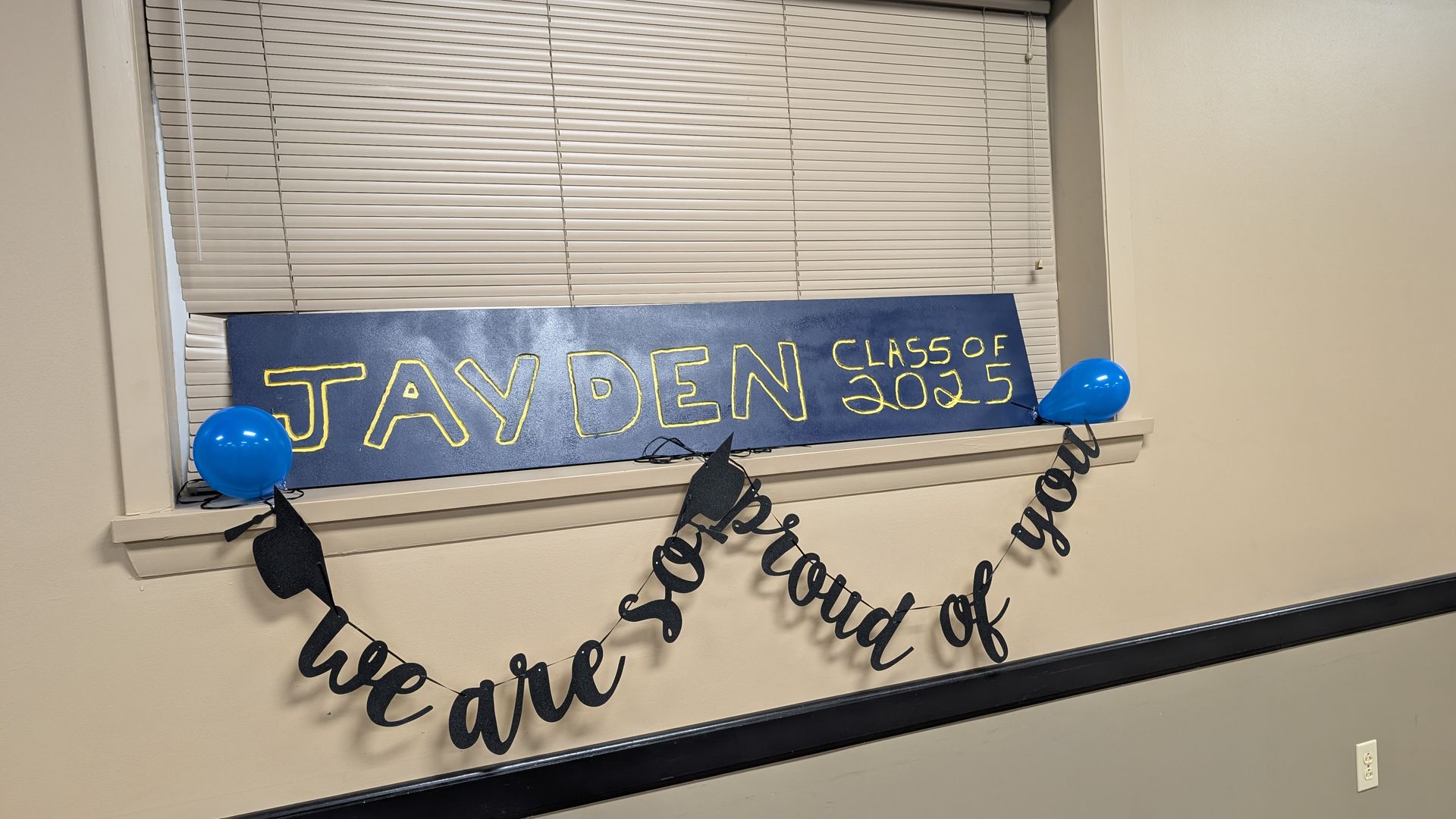 Window with blue “Class of 2023” graduation banner and black “we are proud of you” garland.