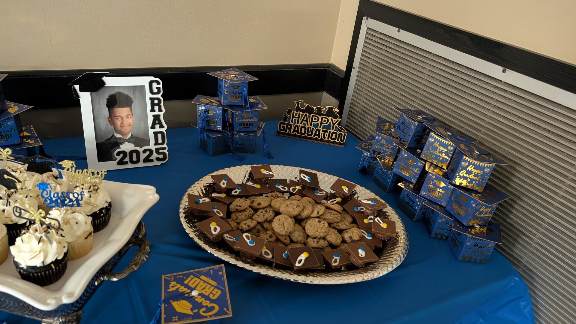Blue graduation dessert table with cake, brownies, candy, and “GRAD 2023” photo display