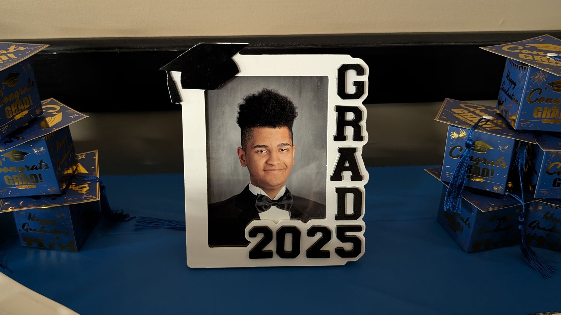 Decorative 2025 graduation display with a portrait and blue-and-gold gift boxes on either side