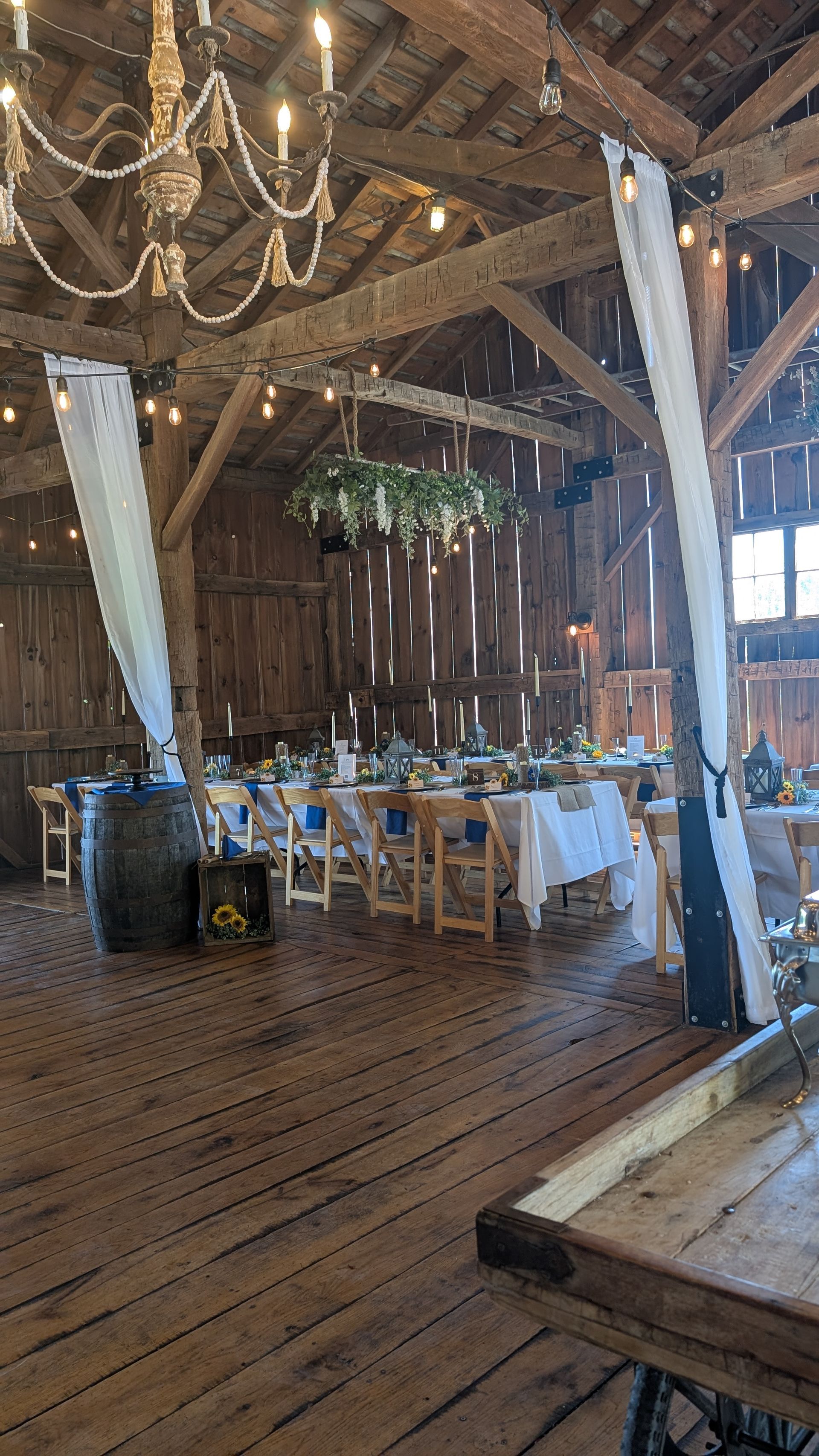 Rustic barn wedding reception with white-draped tables, chandeliers, and wooden beams