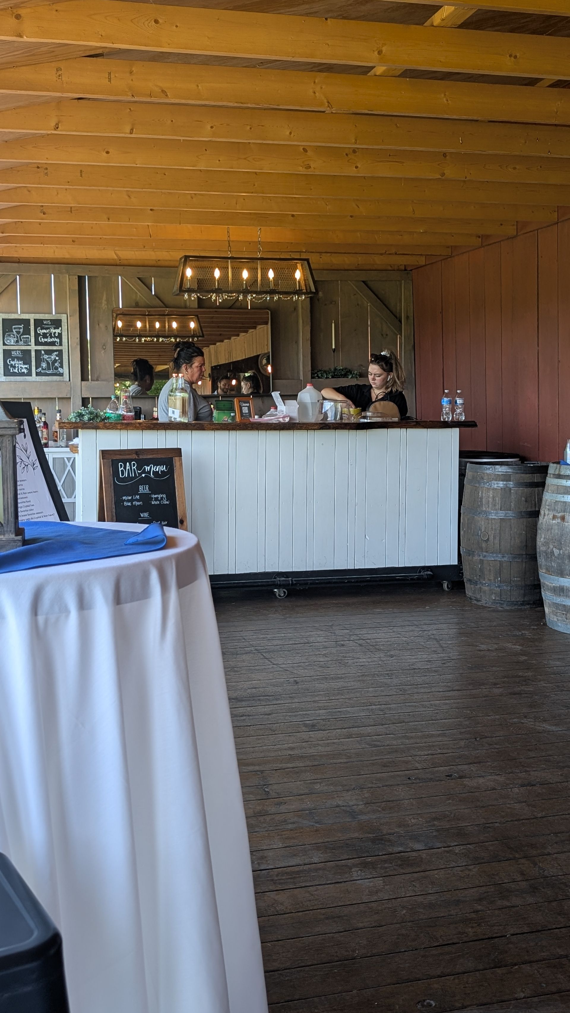 Rustic bar with white counter, bottles, and a staff member behind it in a wood-paneled room