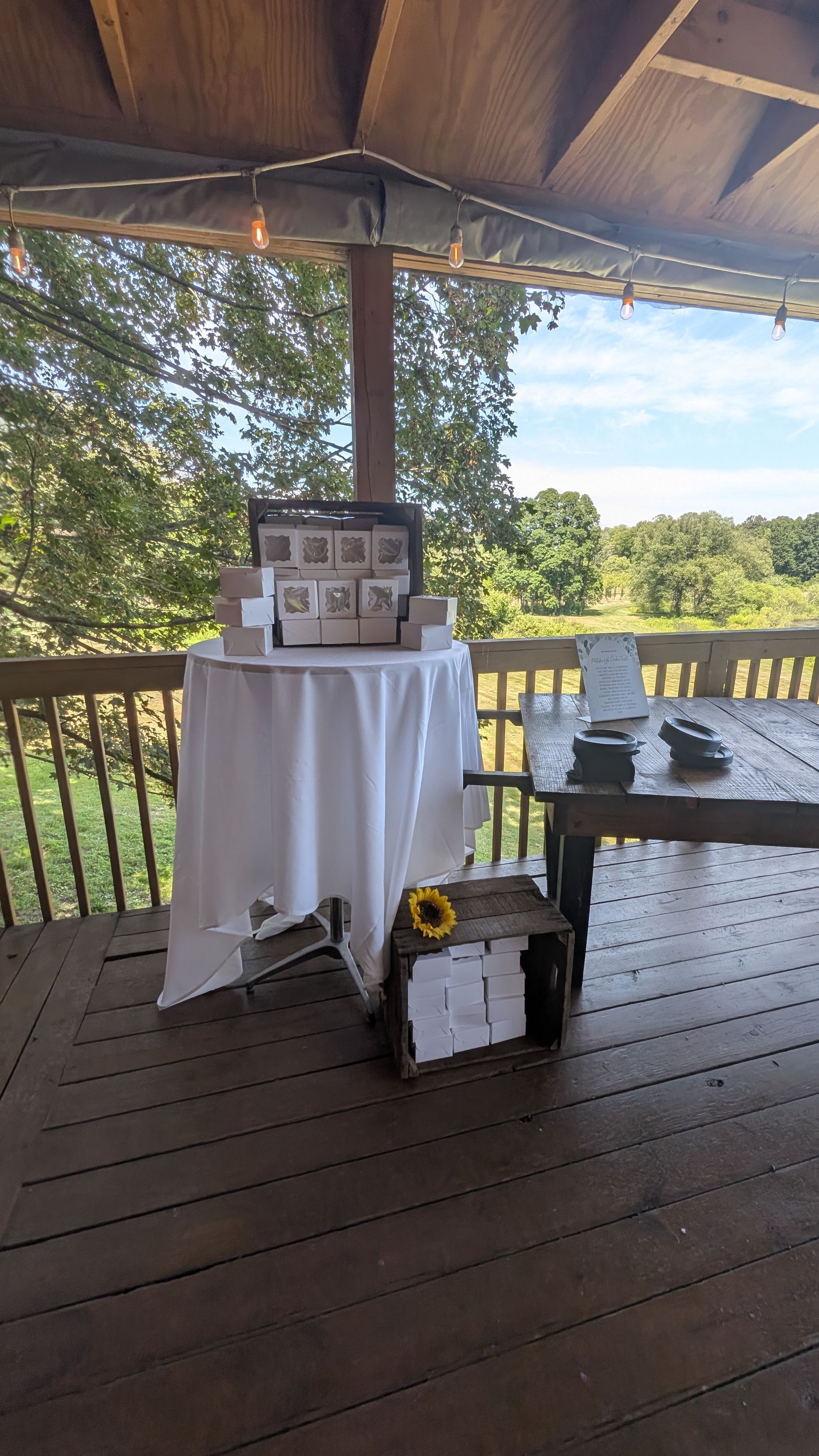 A rustic outdoor deck with a white-draped table displaying boxes and a black case near the railing.