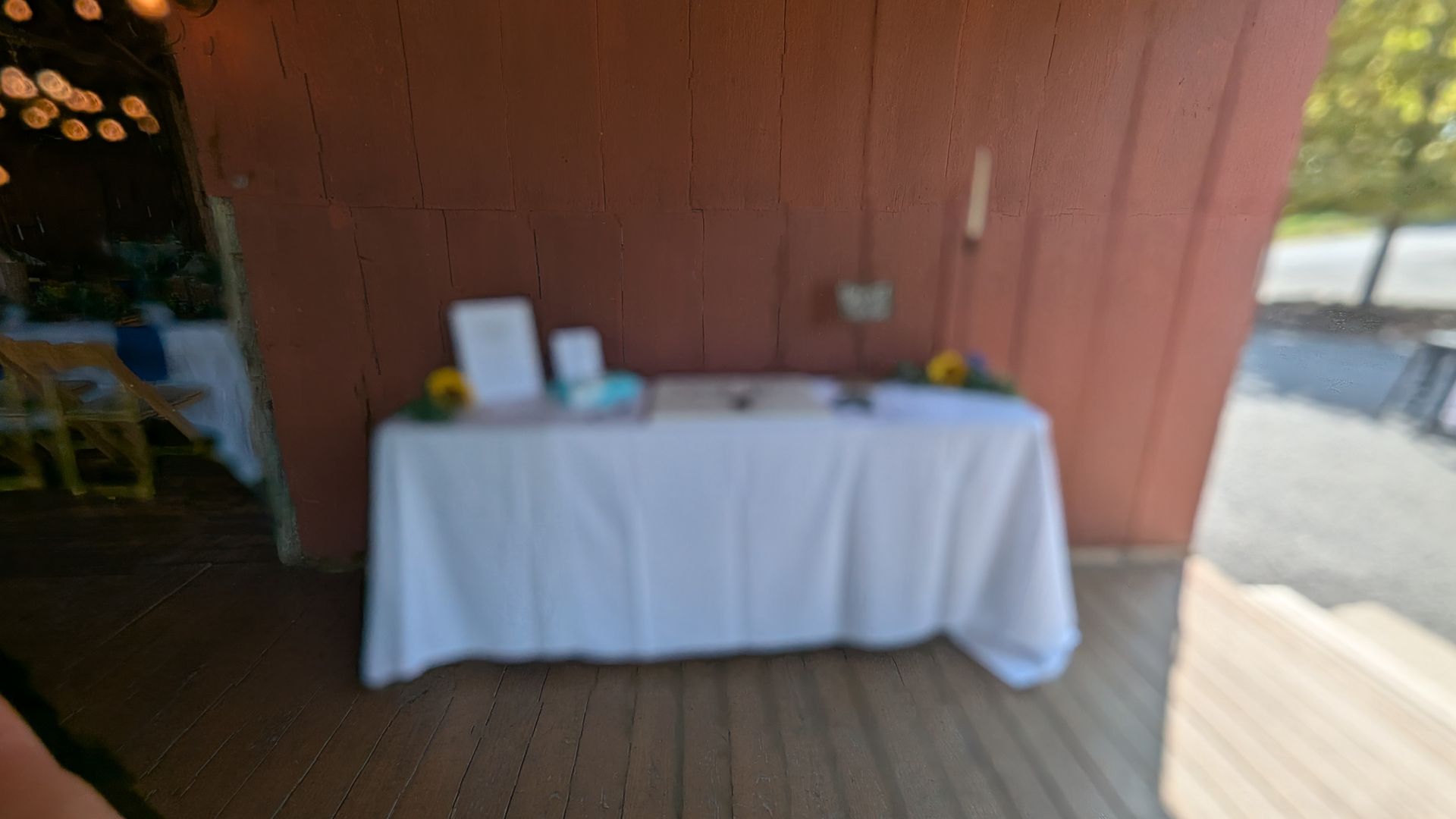 White-clothed table with signs and items against a red wall on a wooden patio
