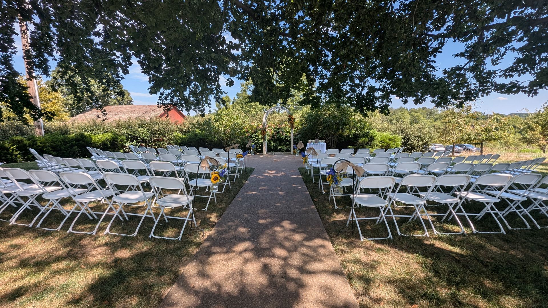Outdoor ceremony setup with white chairs lining a central aisle under trees
