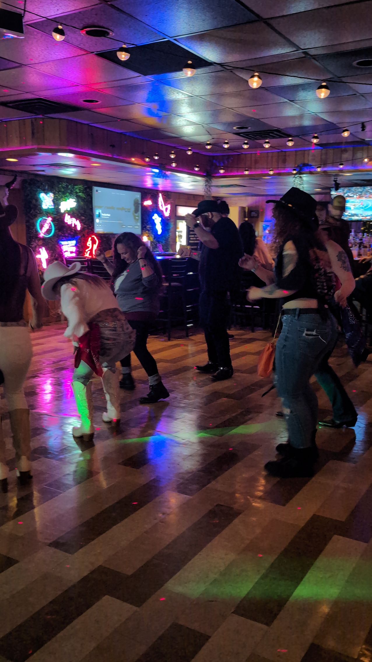 People dancing in a neon-lit club with colorful reflections on the floor.