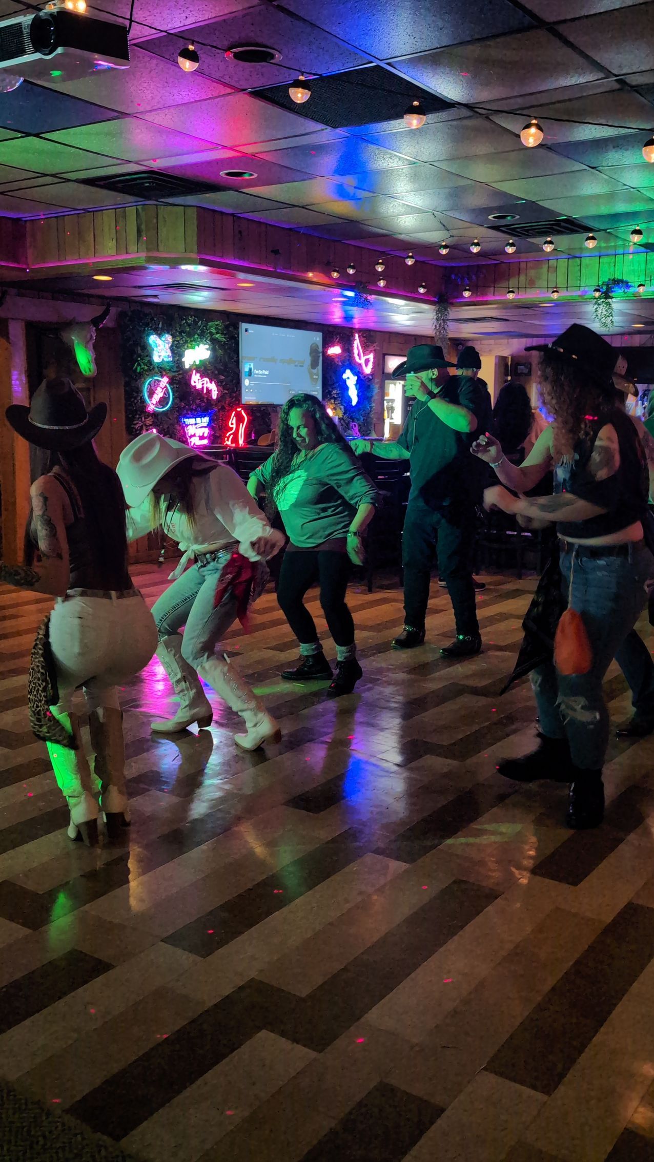 People dancing in a dimly lit club with colorful neon lights and a mirrored ceiling