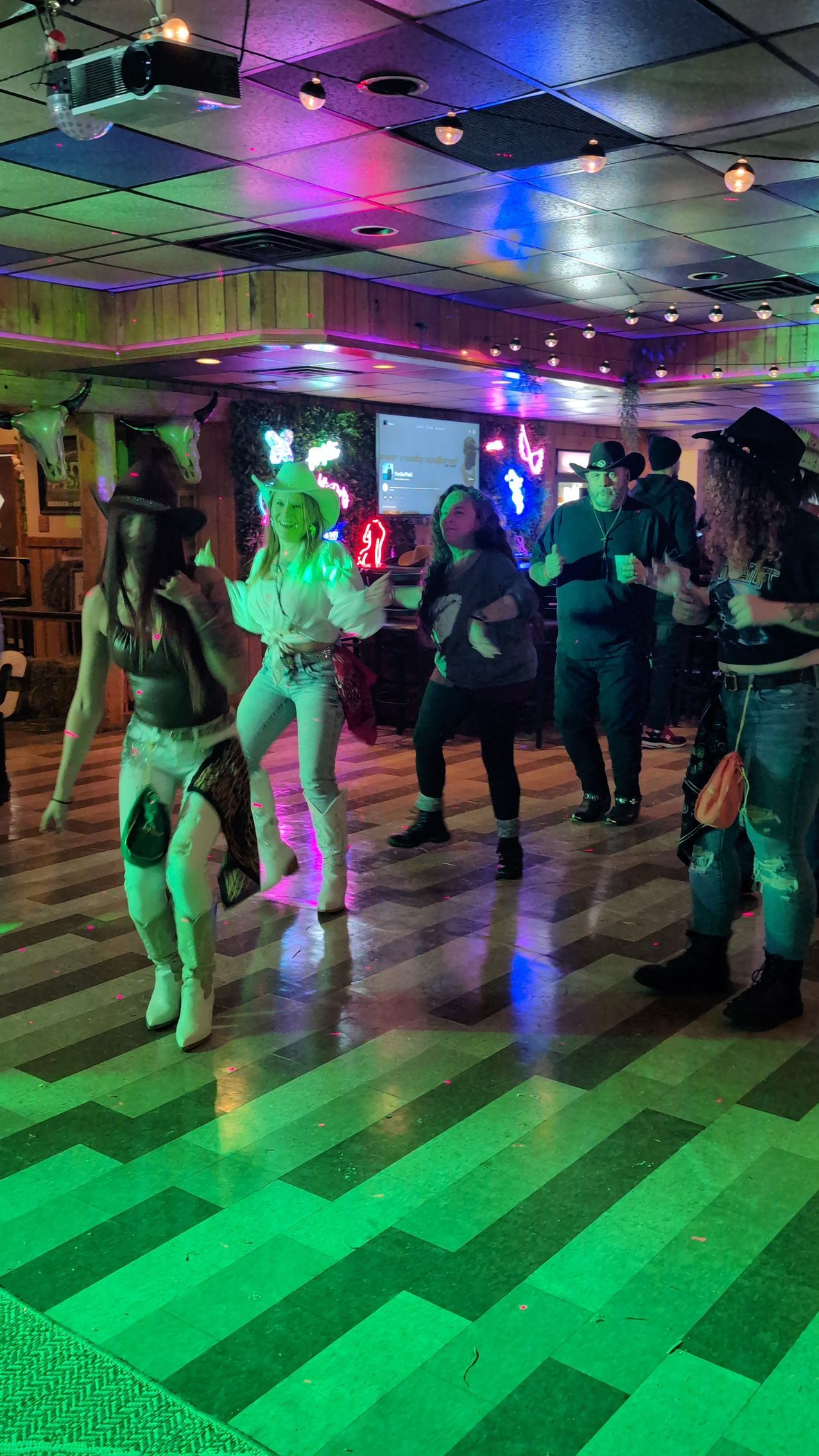 People dancing in a dimly lit club with colorful neon lights and a checkered floor.