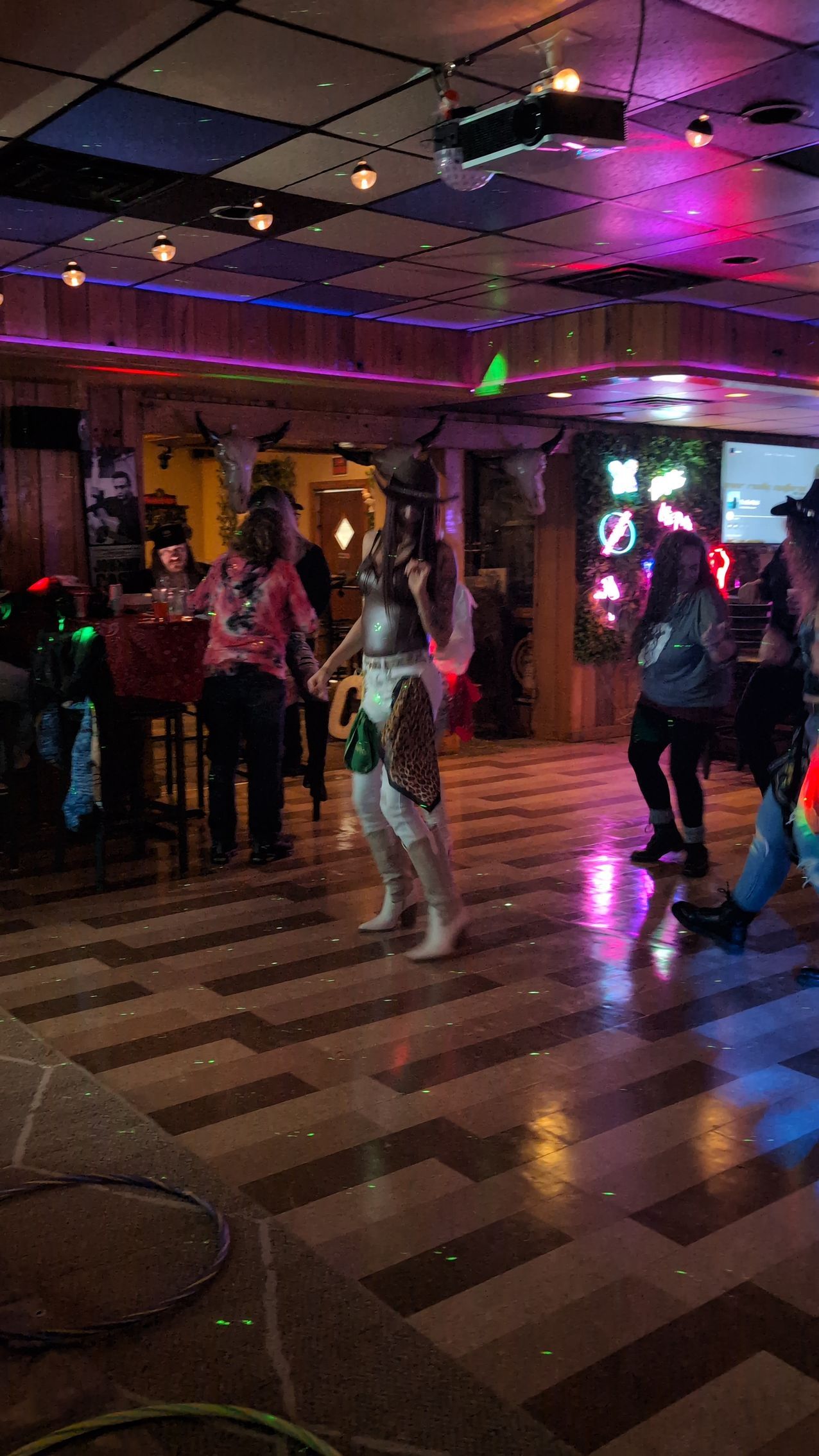 People dancing in a dimly lit club with colorful neon lights and reflective floor