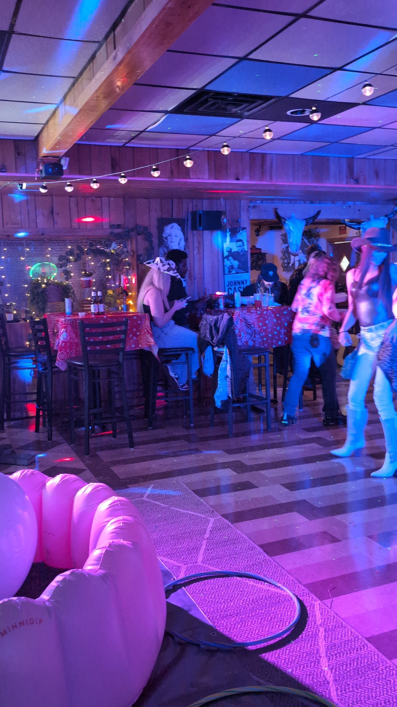 People dancing in a neon-lit nightclub with purple lighting and a tiled floor