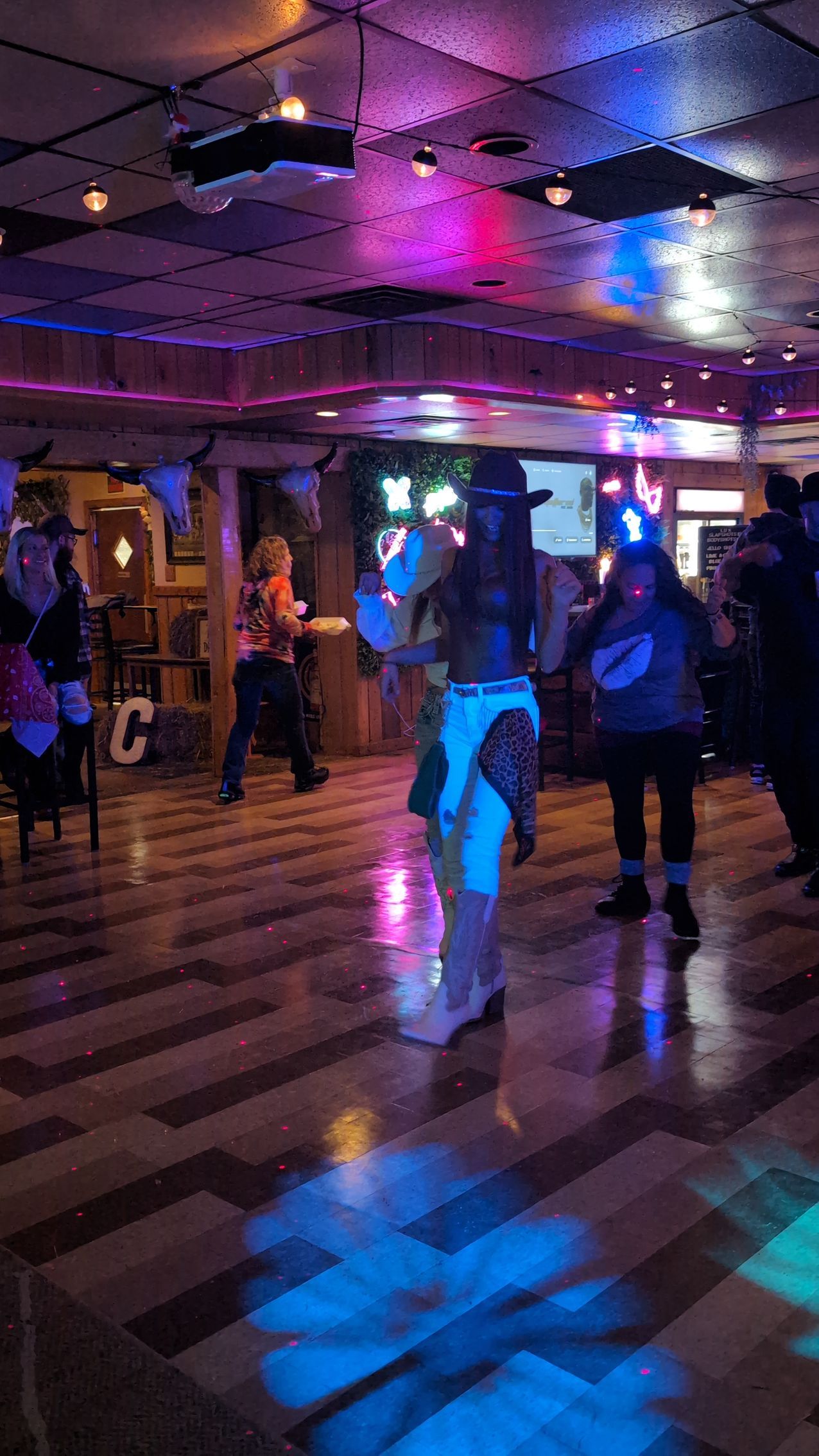 People dancing in a neon-lit nightclub with colorful reflections on the floor