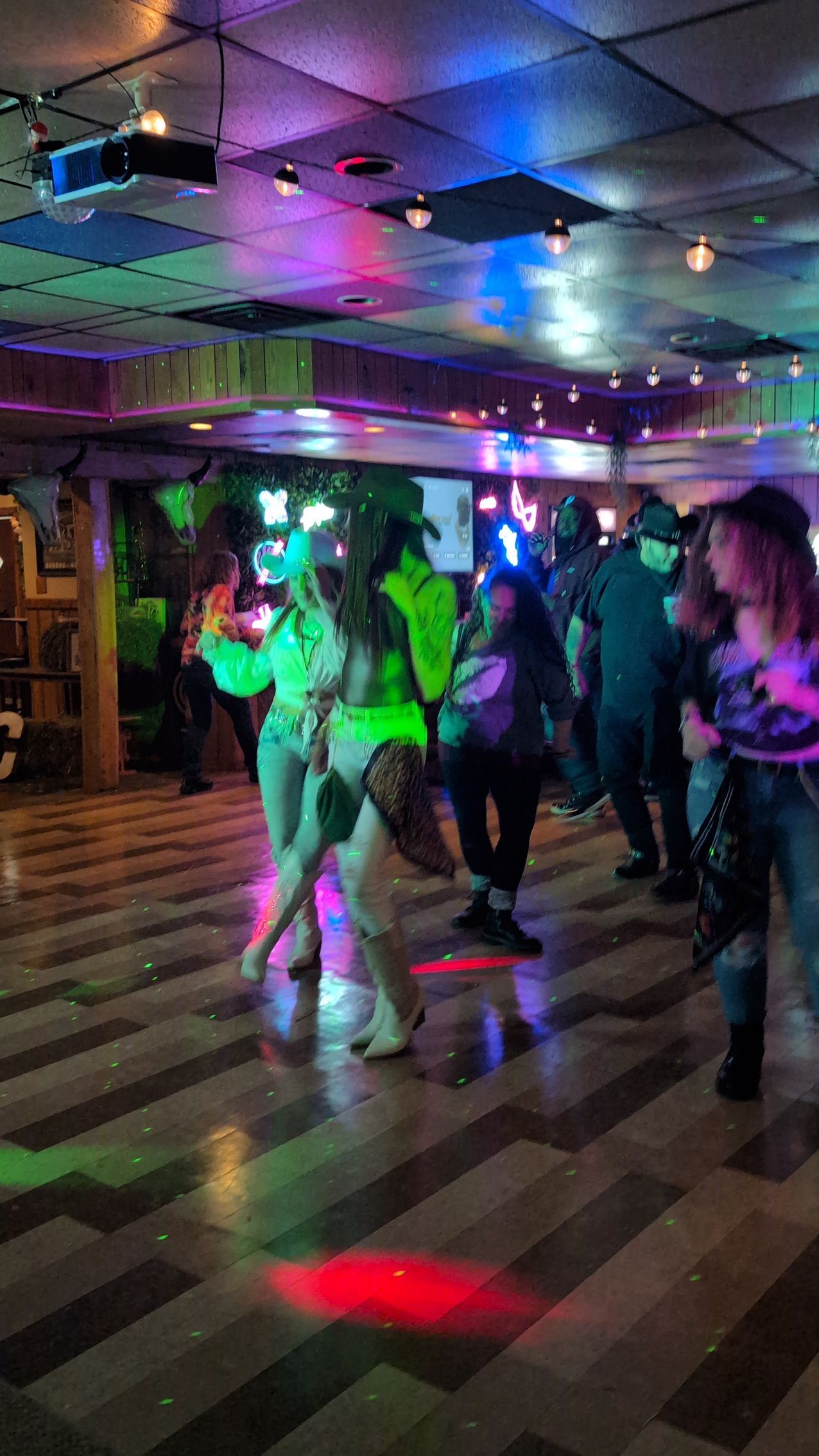 People dancing in a dimly lit room with colorful neon lights reflecting on the floor.