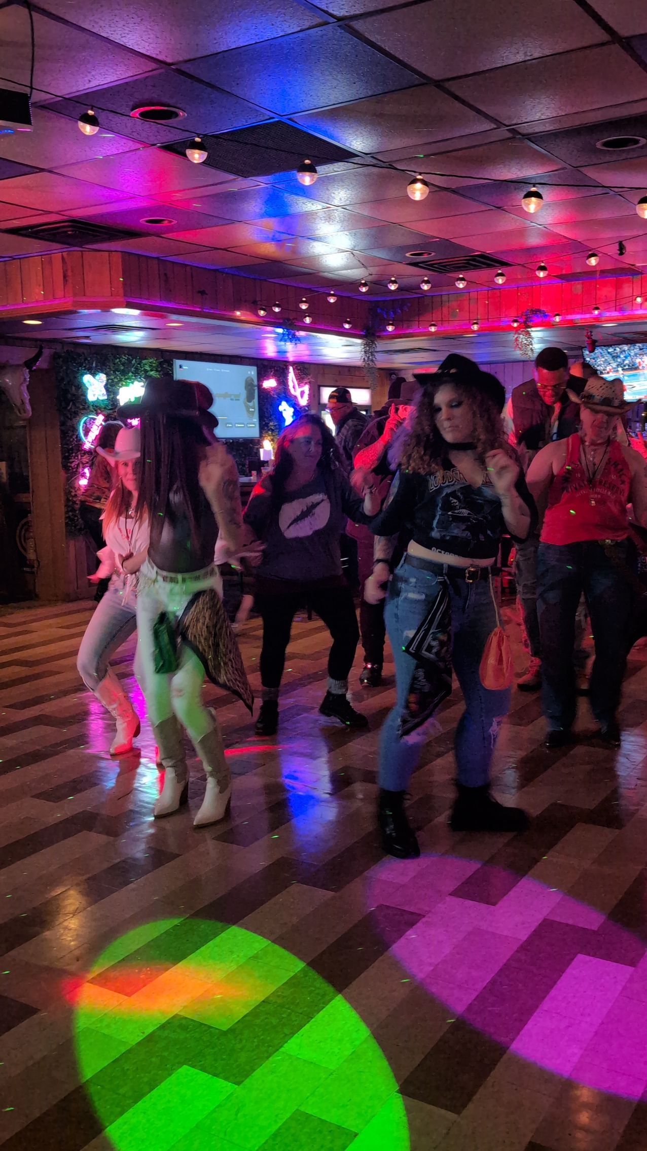 People dancing in a dim nightclub with colorful pink, purple, and green lights on the floor.