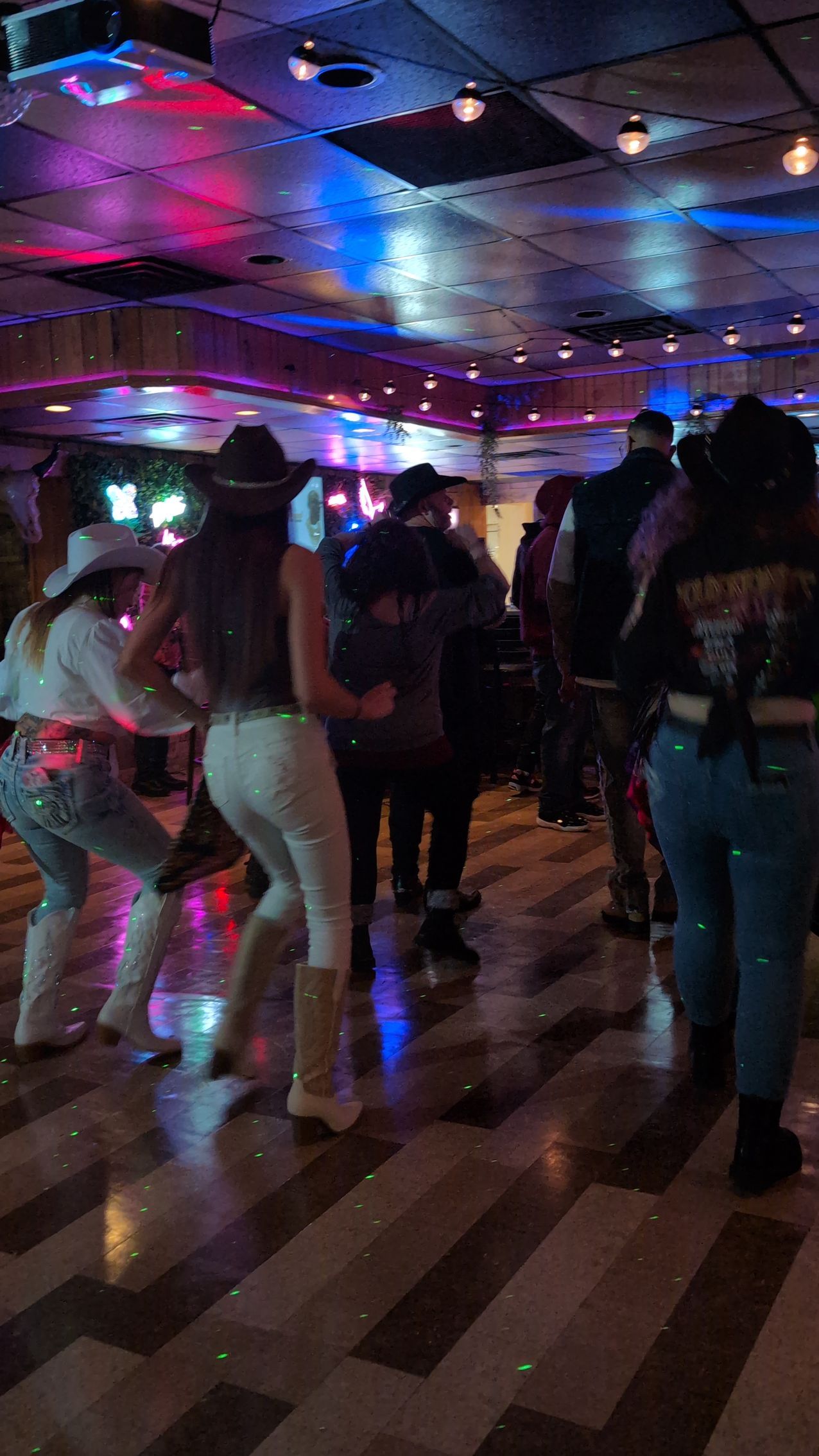 People dancing in a dimly lit club with colorful purple and blue lights reflecting on the floor.