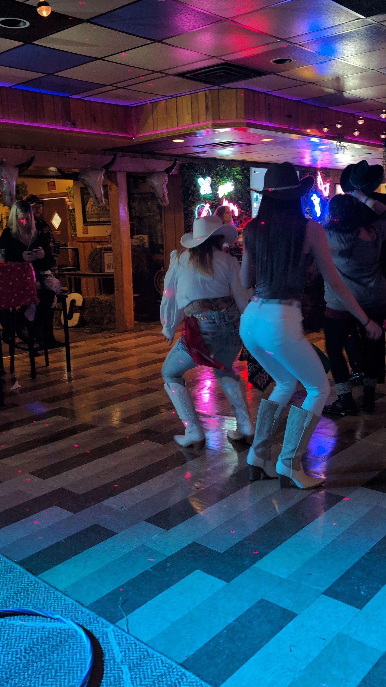 People dancing in a dimly lit nightclub with colorful neon lights and a checkered floor