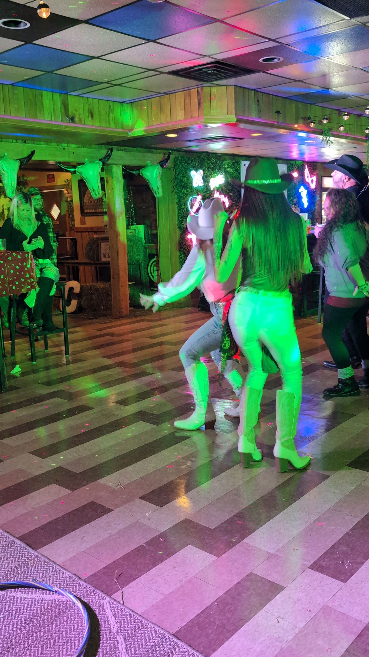 People dancing in a neon-lit nightclub with a checkered floor and colorful ceiling lights
