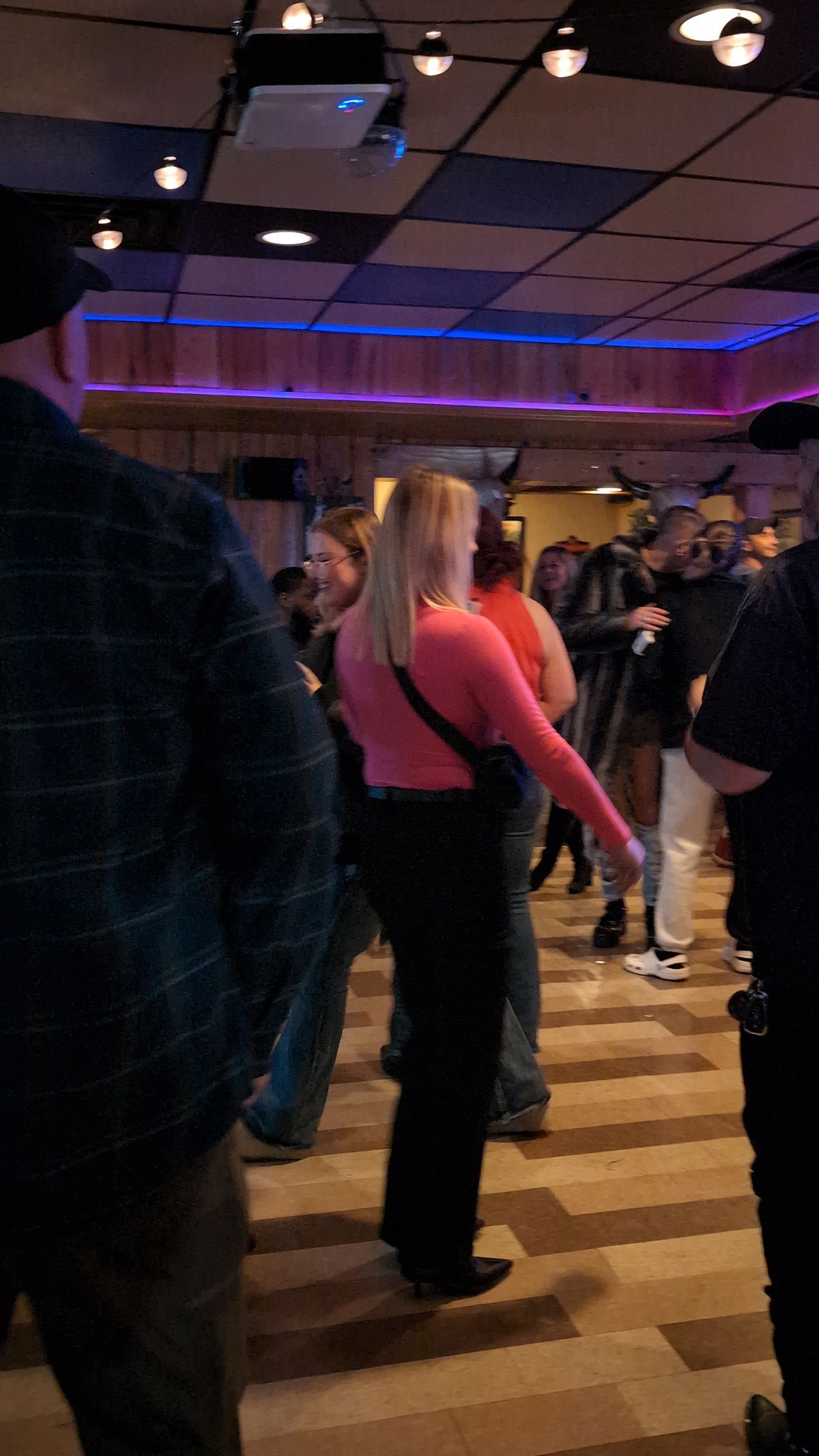 People dancing in a dimly lit room with purple accent lights and a checkered floor.