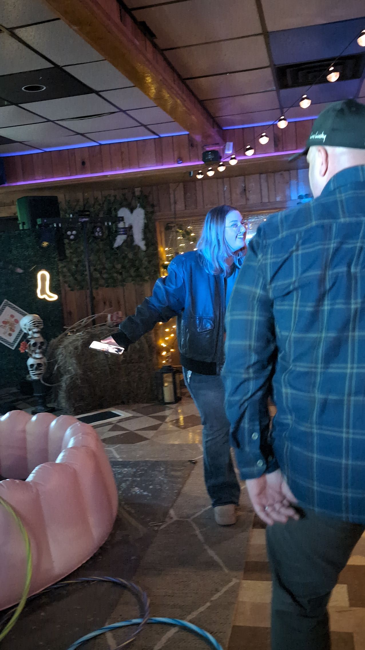 People walking through a neon-lit indoor venue with a wooden ceiling and tiled floor.